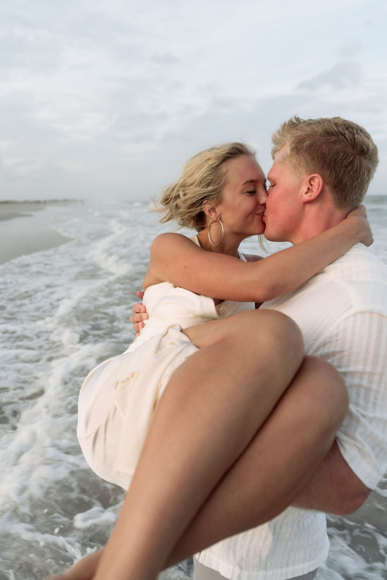 A romantic couple shares a passionate kiss while standing near the ocean waves.