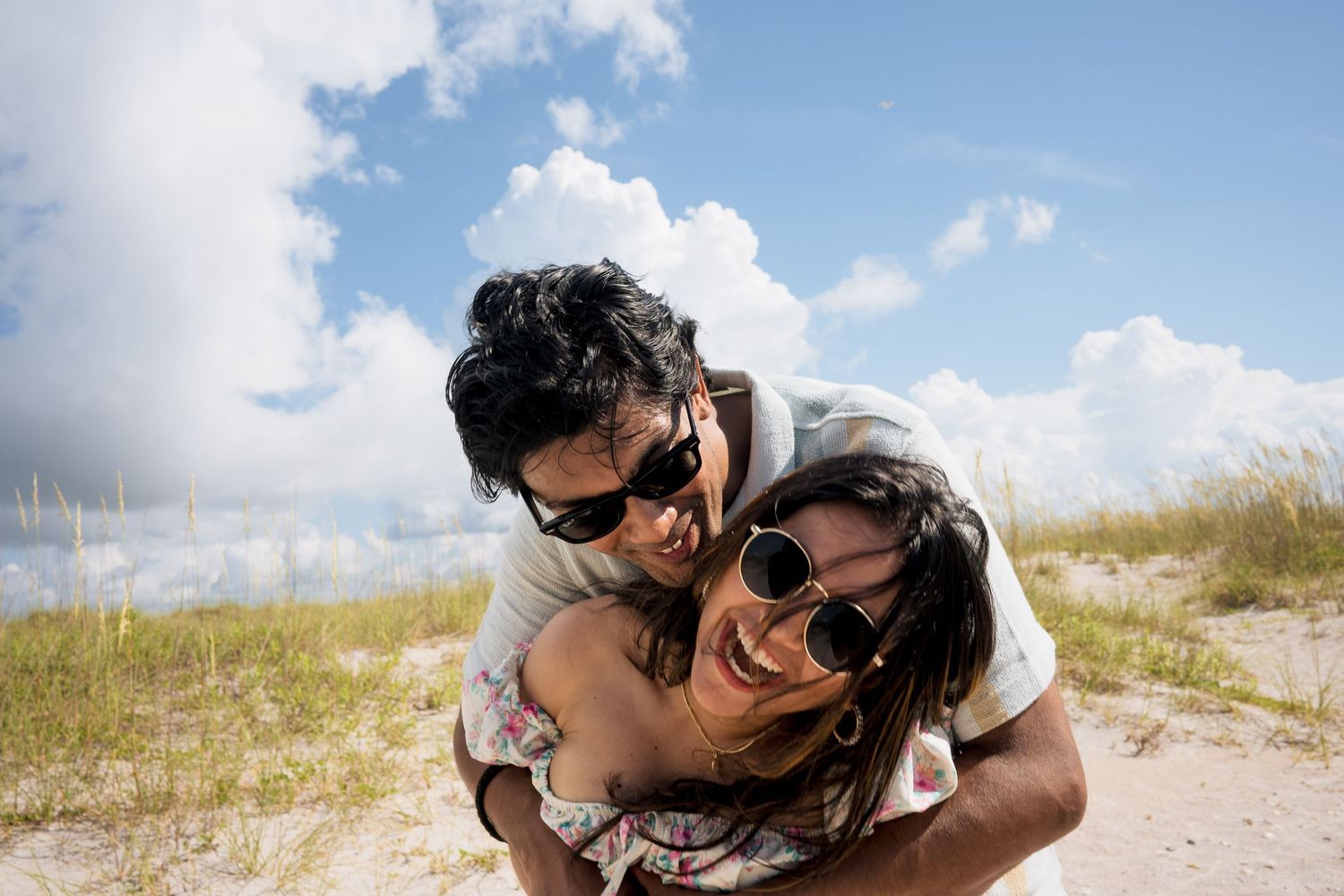 Two people share a romantic moment together on a sandy beach with blue skies overhead.