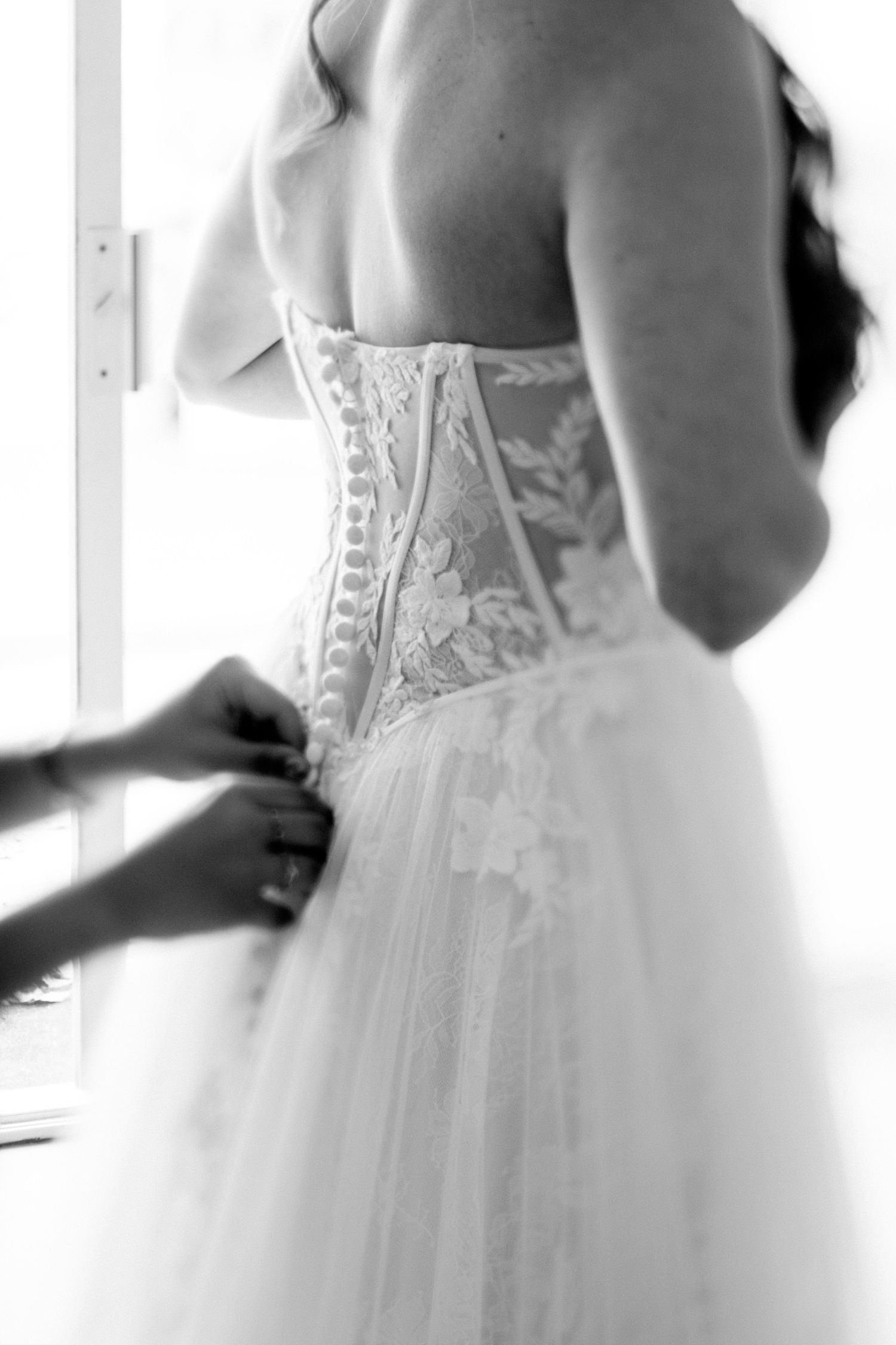 Black and white close-up view of a wedding dress with intricate corset back lacing and a flowing tulle skirt.