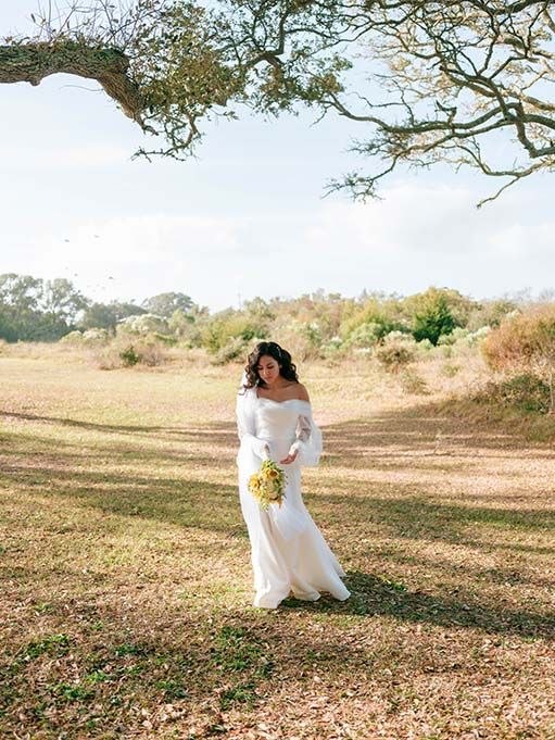 A couple in white wedding attire shares romantic moments in a sunlit meadow with scattered autumn leaves.