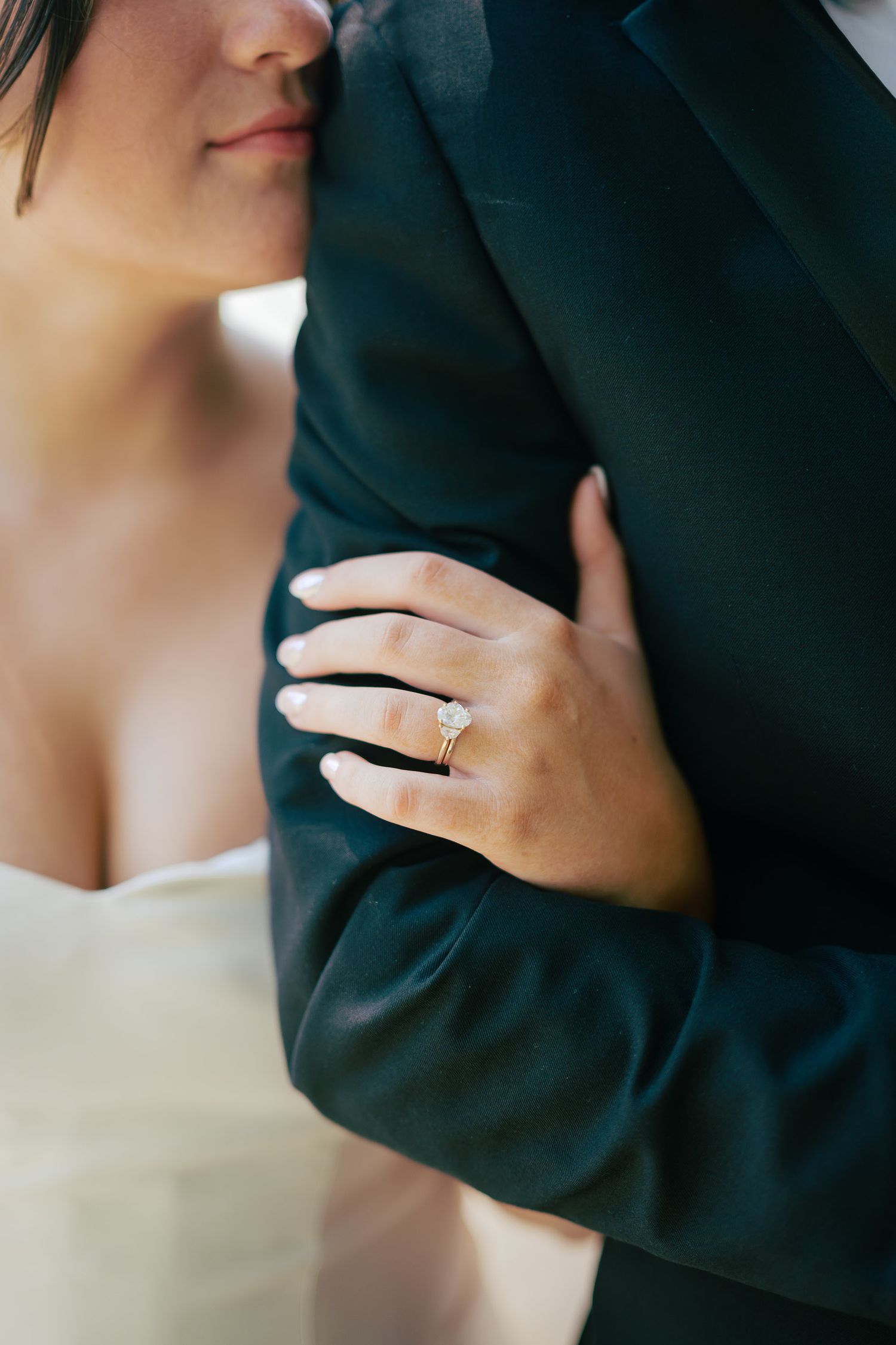 Close-up of bride holding groom's arm, showcasing a stunning diamond solitaire engagement ring on her finger.