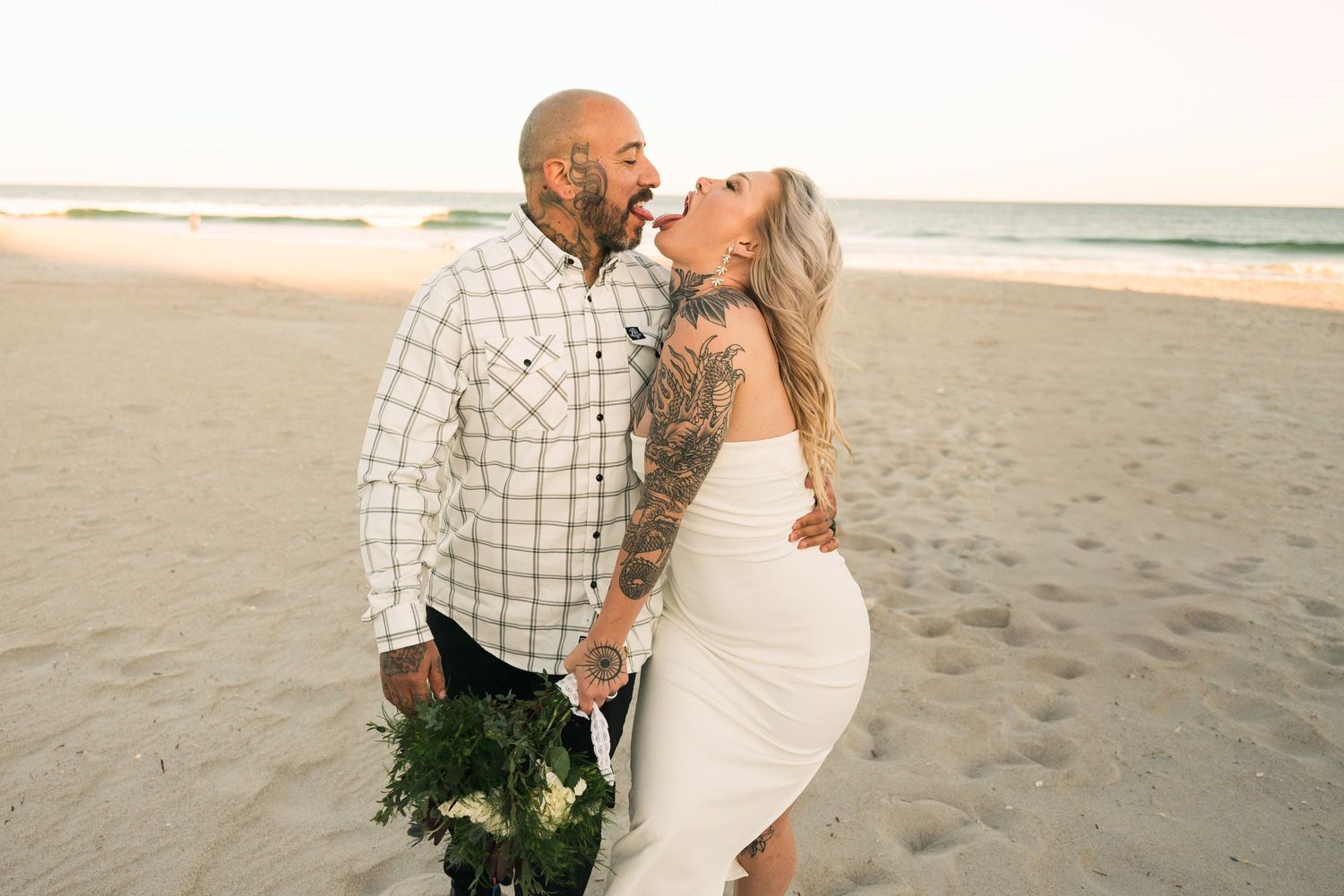 A couple laughs together during a romantic photo session on a sandy beach at sunset.