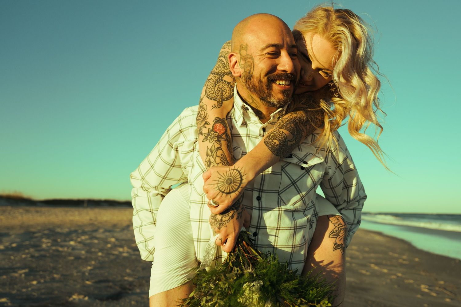 A couple shares a romantic moment together on a sandy beach at sunset with turquoise water in the background.