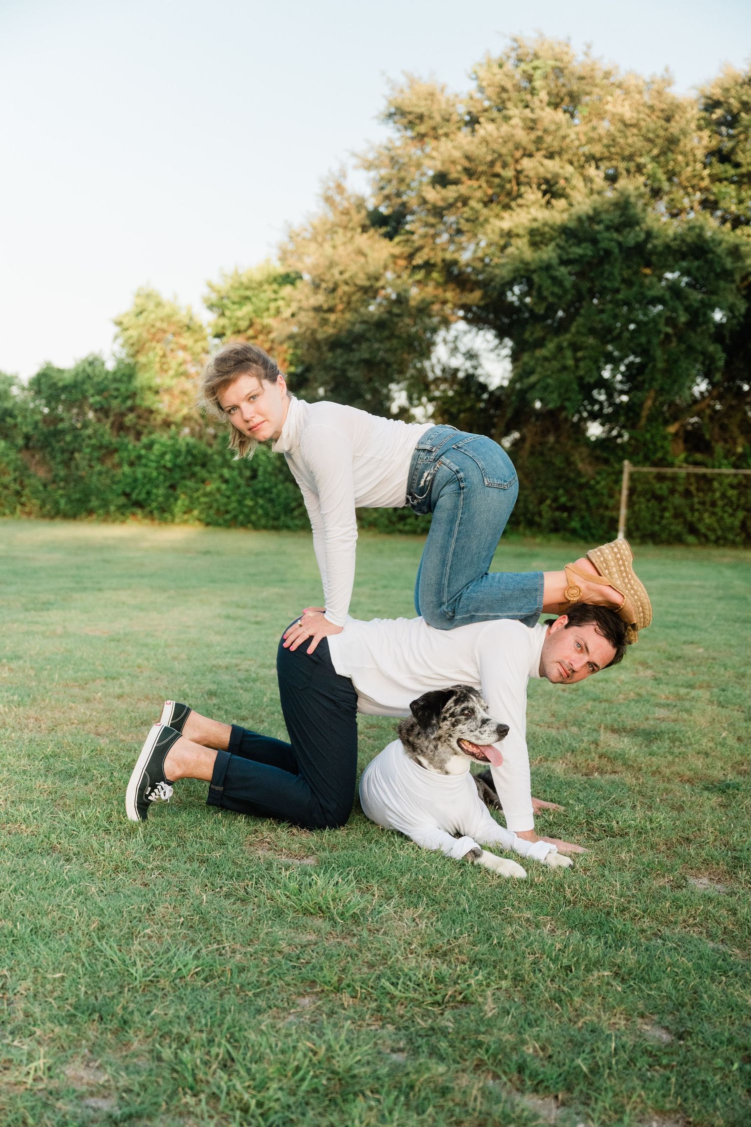 A person and their Australian Shepherd dog play and interact together on a grassy field during a sunny day.