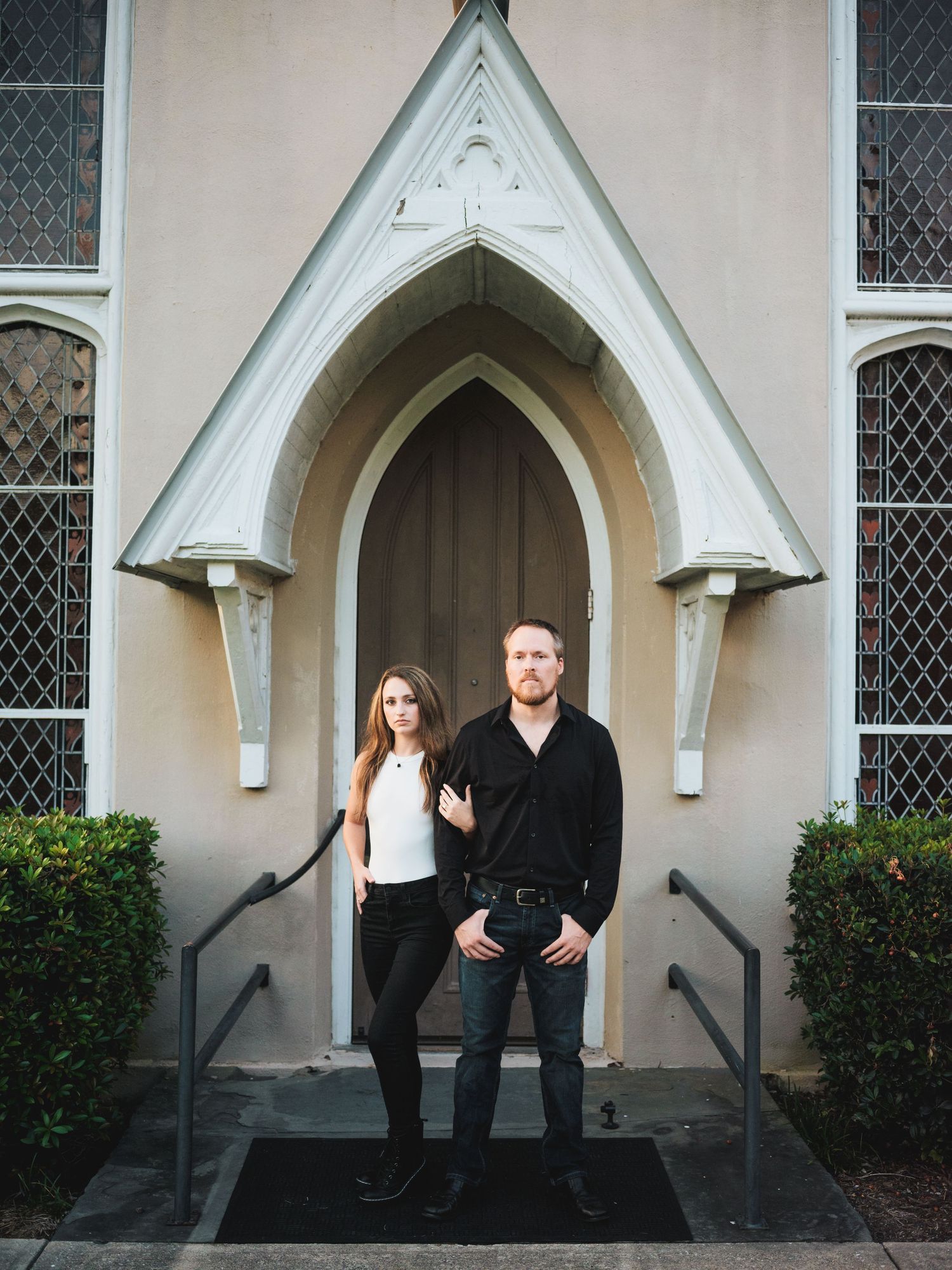 A couple stands in front of a Gothic church doorway with pointed arch architecture in beige and white.