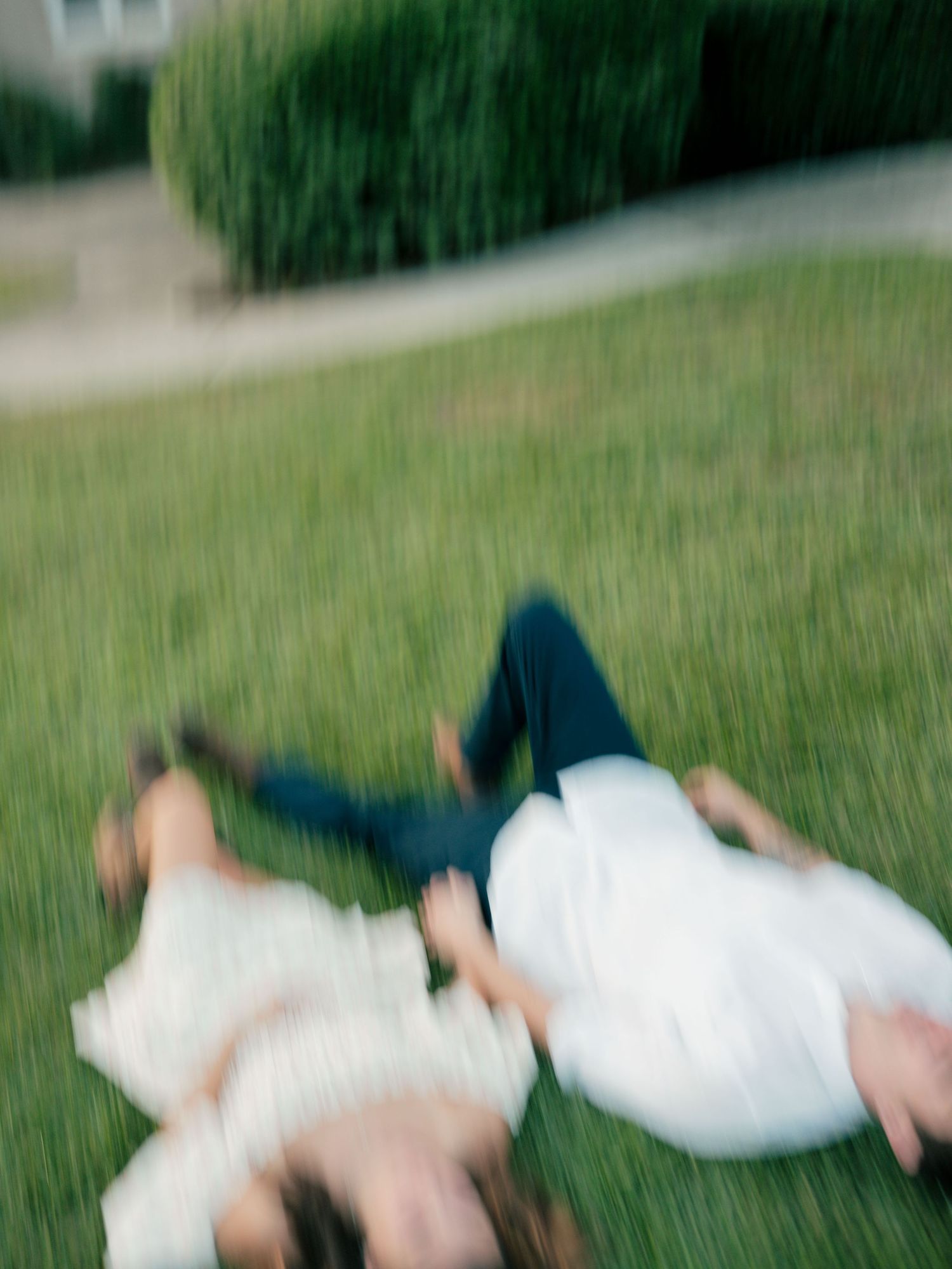 Motion-blurred image of two people lying on grass with one wearing white and one wearing dark clothing.
