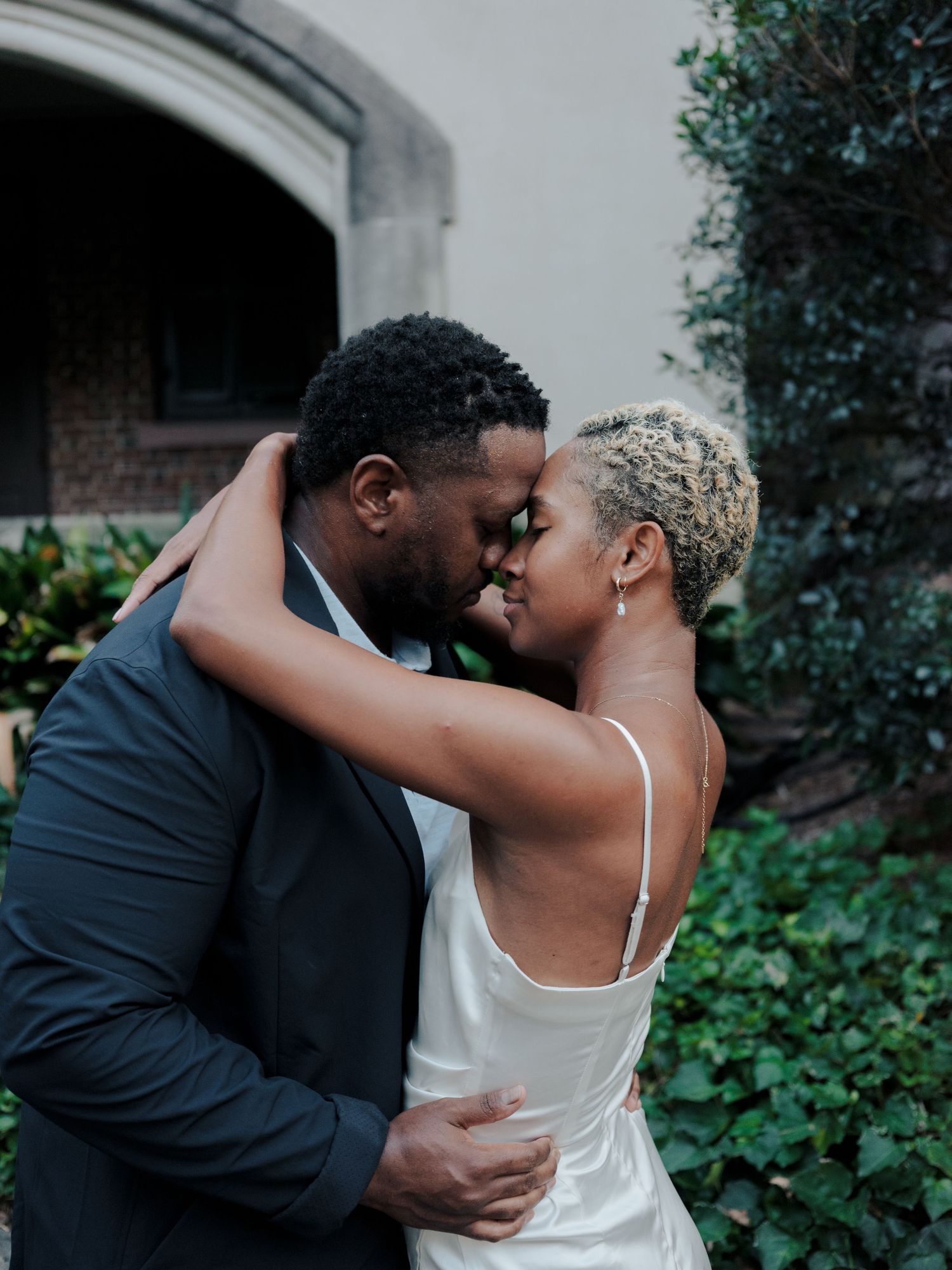 A romantic couple embraces intimately in a garden setting with a pastel background.