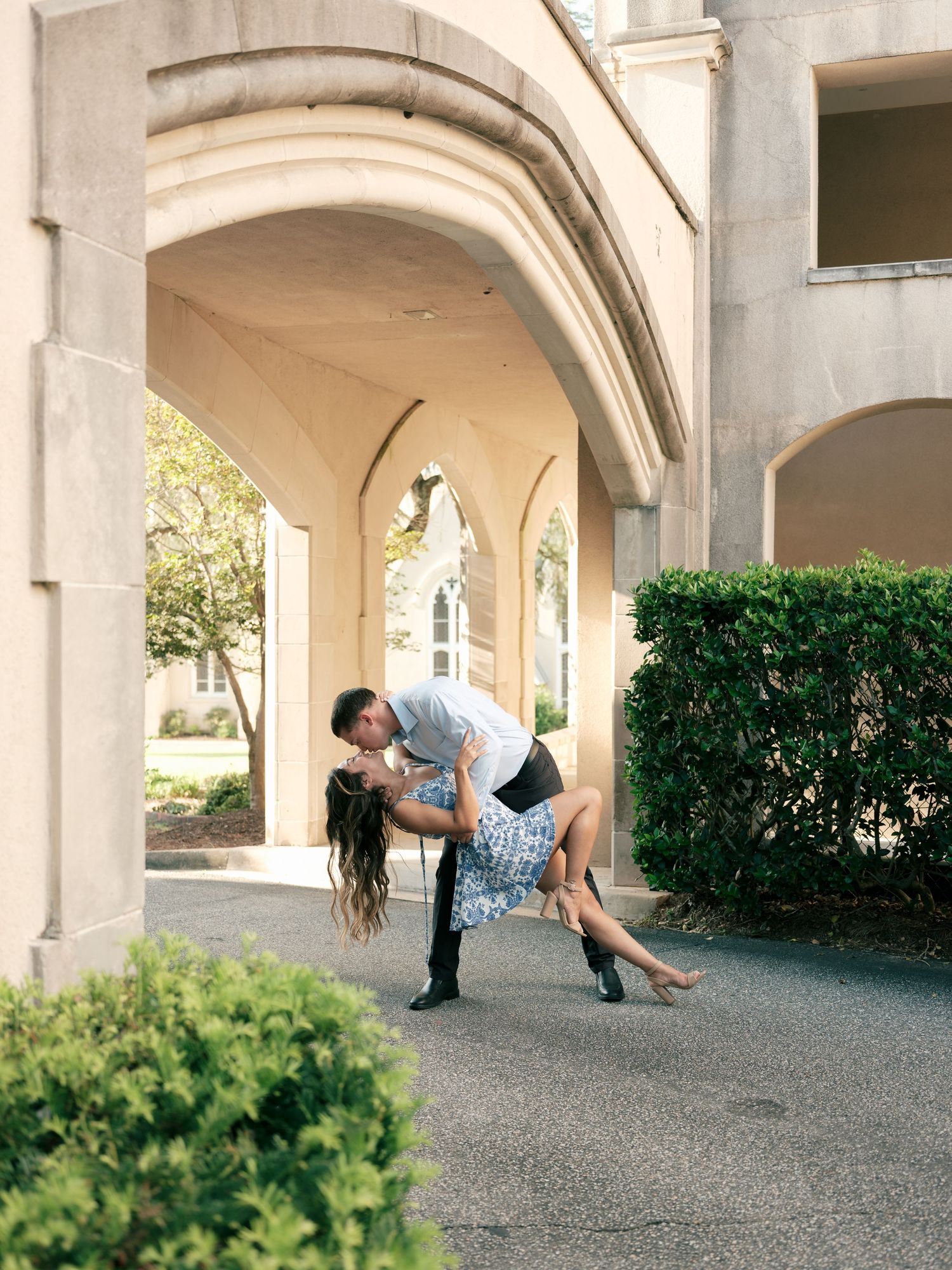 Romantic dance dip under stone archway with decorative landscaping at elegant venue entrance.