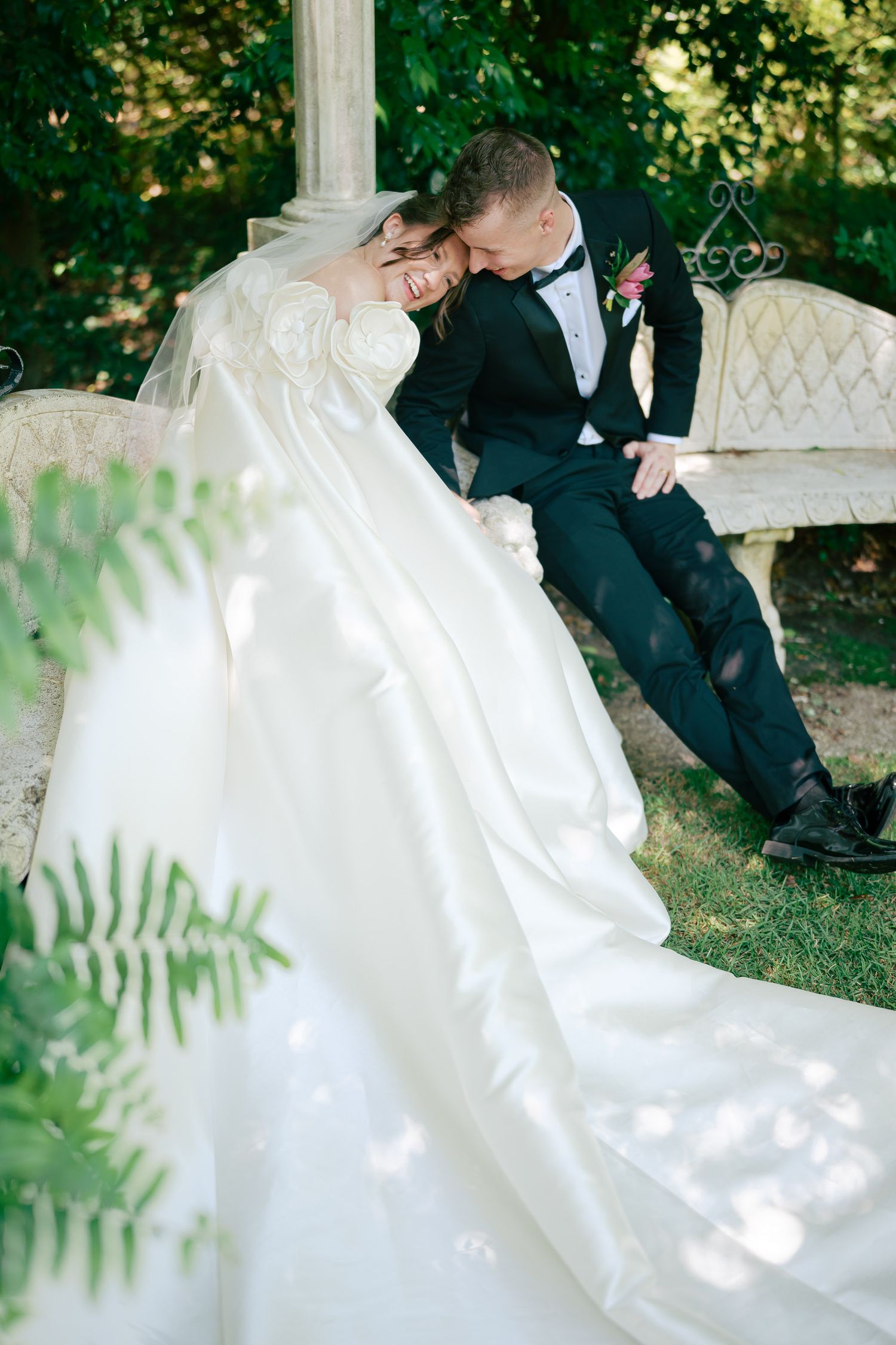 Bride and groom sharing a romantic moment on a garden bench, bride in flowing white gown, groom in black tuxedo.