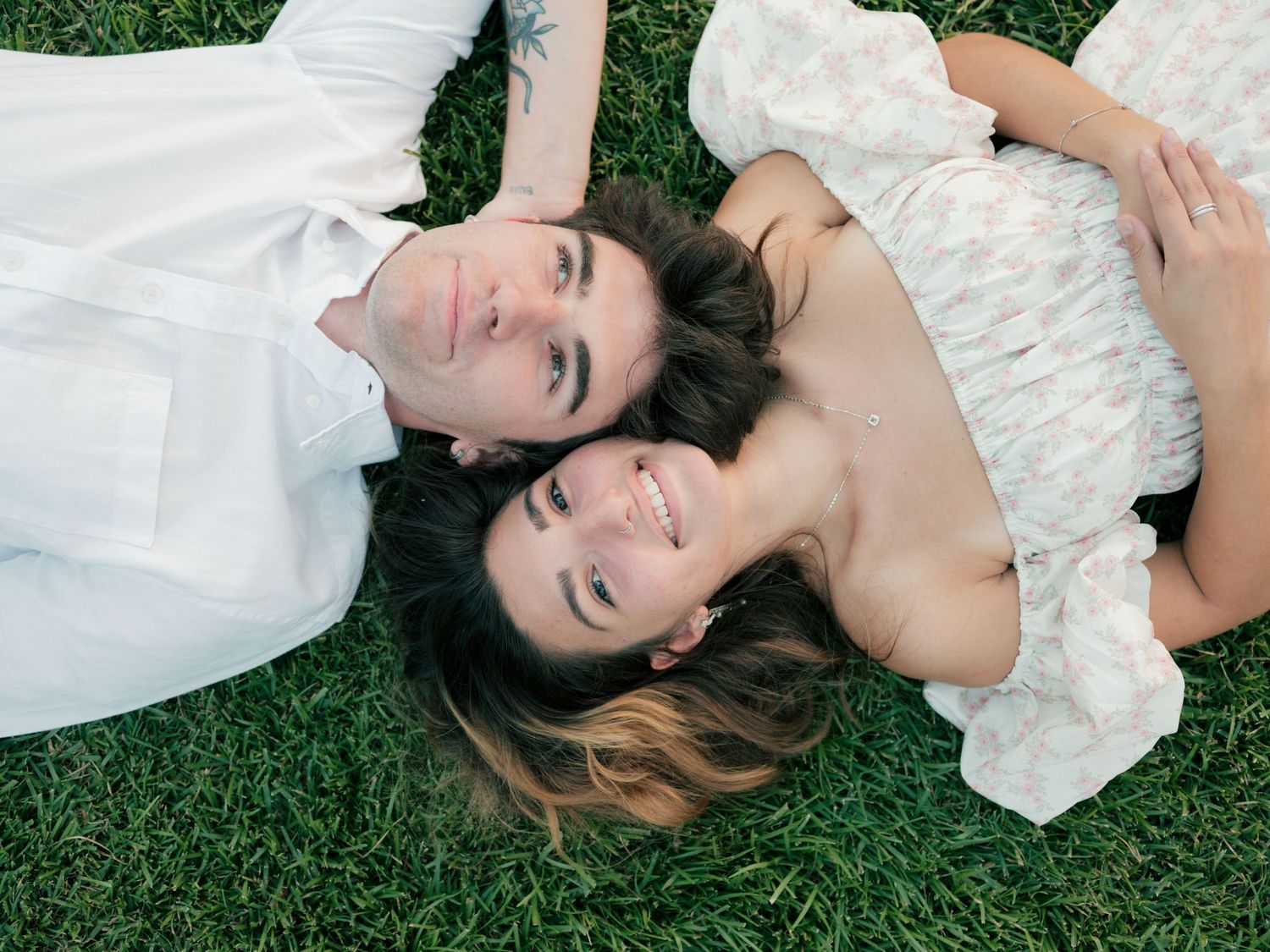 A person in a white wedding dress lies on lush green grass while posing for romantic outdoor portraits.