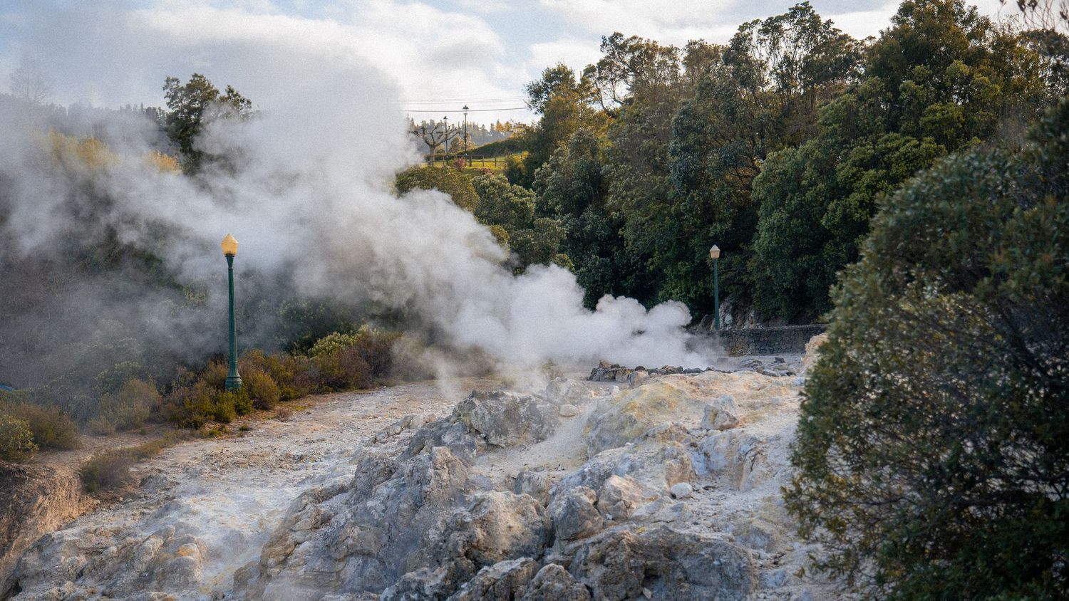 A series of steaming geysers and hot springs emit white vapor into the air at a geothermal park.