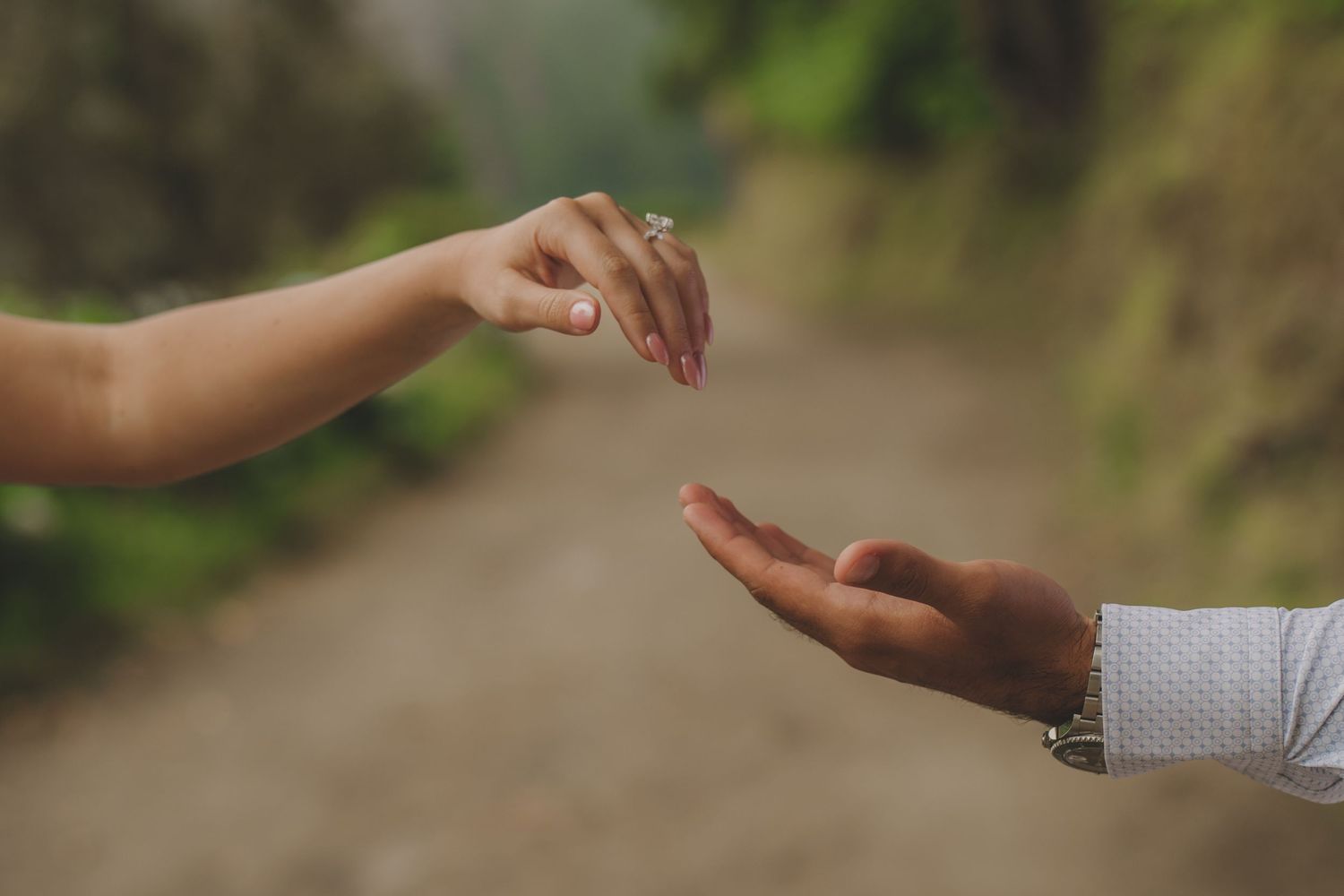 Close-up of hands releasing something into the air against a blurred natural background.