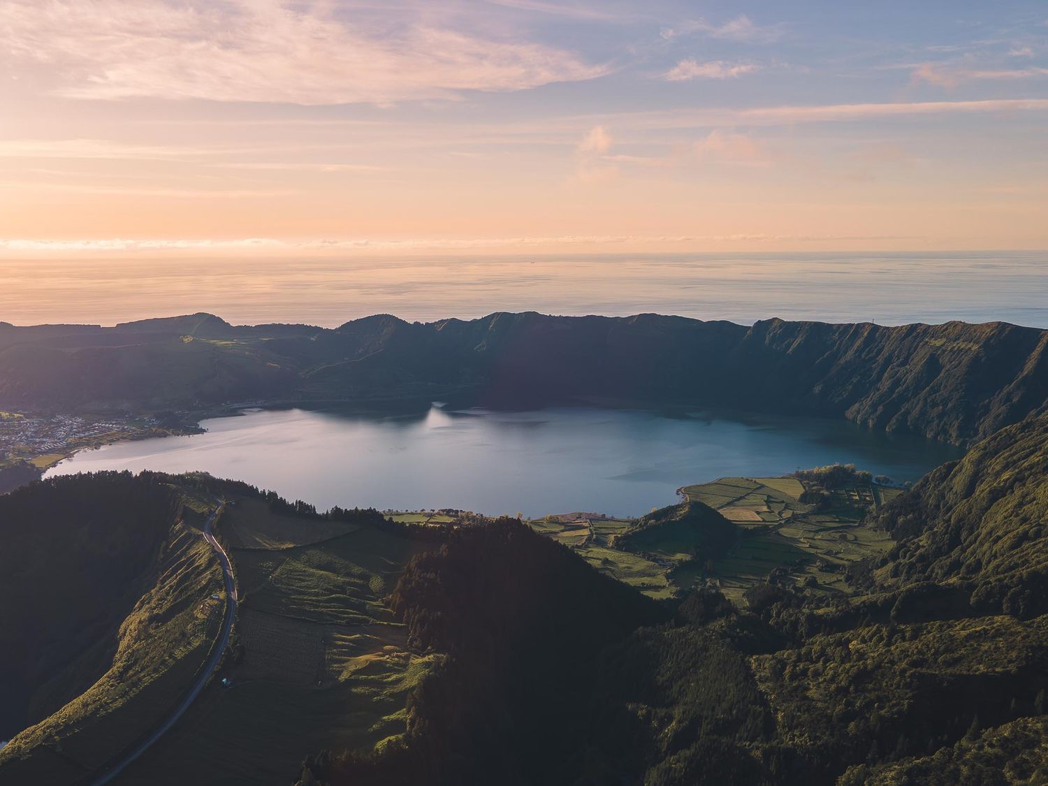 Aerial view of serene mountain caldera lake surrounded by green slopes during sunset with pink skies.
