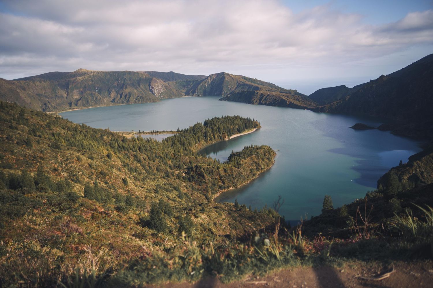 Aerial view of Sete Cidades volcanic crater lake with green peninsula jutting into turquoise waters on Sao Miguel island.