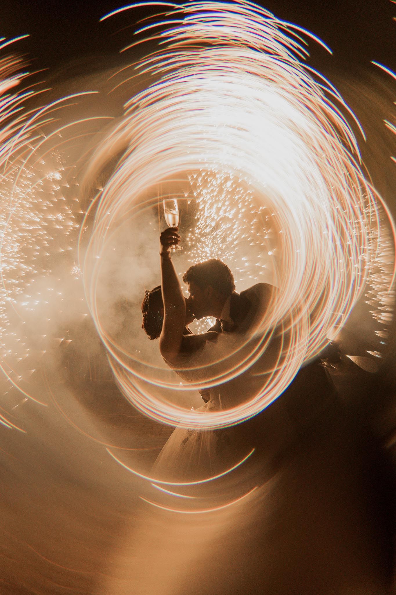 Long exposure photograph showing spiraling light trails of fire performers creating circular patterns against dark background.