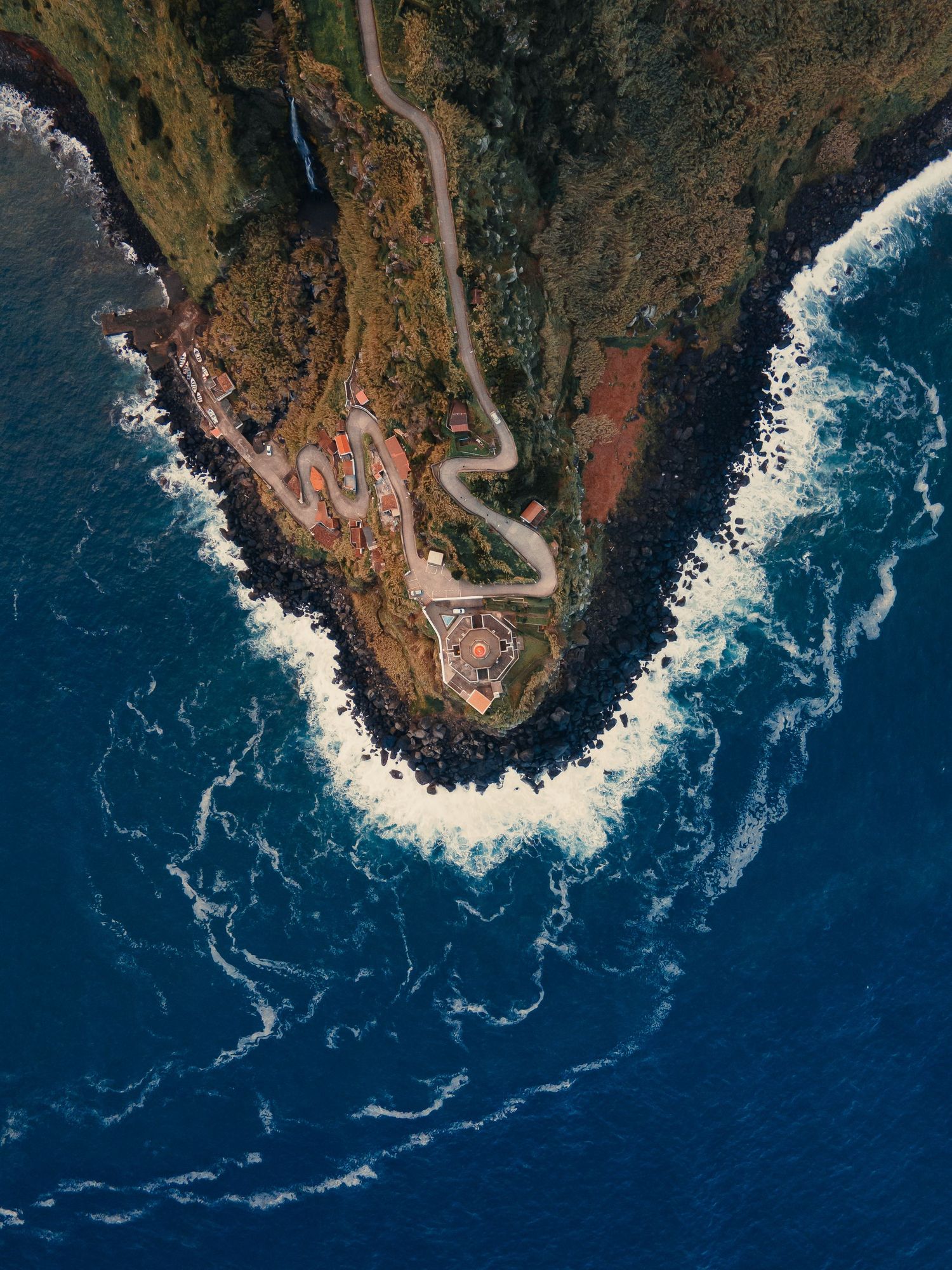 Aerial view of a winding coastal road along dramatic cliffs with crashing waves against rocky shores.