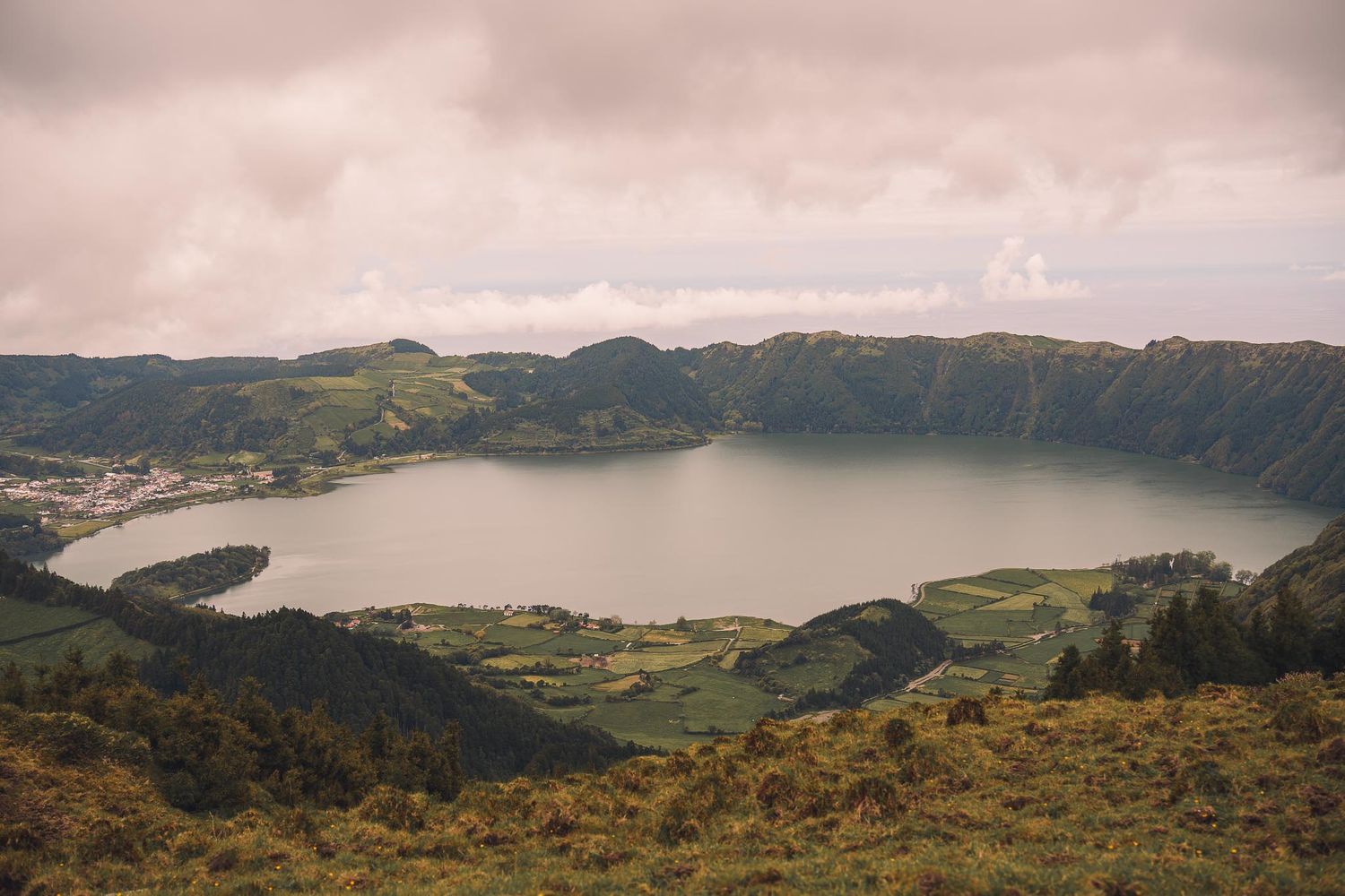 Misty view of crater lakes and volcanic terrain in the Azores with dramatic cloud cover.