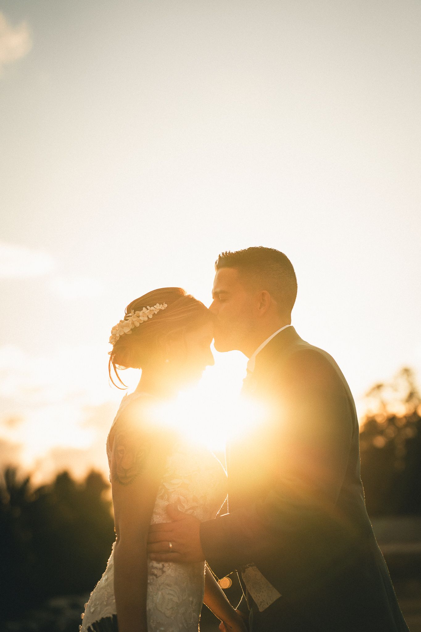 Silhouetted couple shares a romantic moment at sunset with sunflare creating a dreamy golden glow.