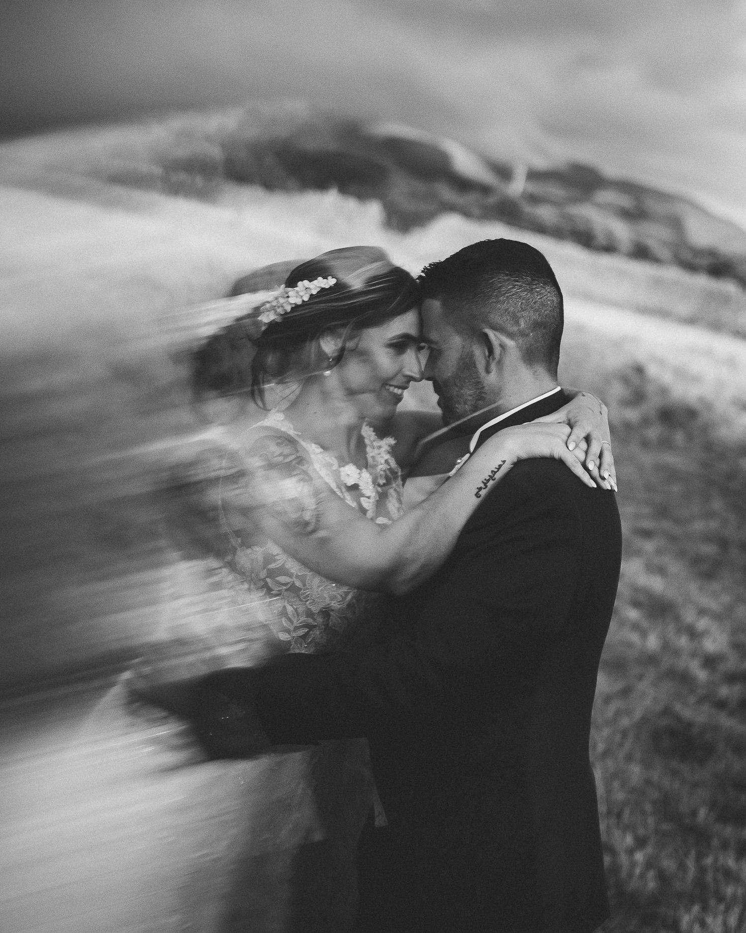 A black and white artistic wedding portrait showing a romantic embrace on a misty hilltop.