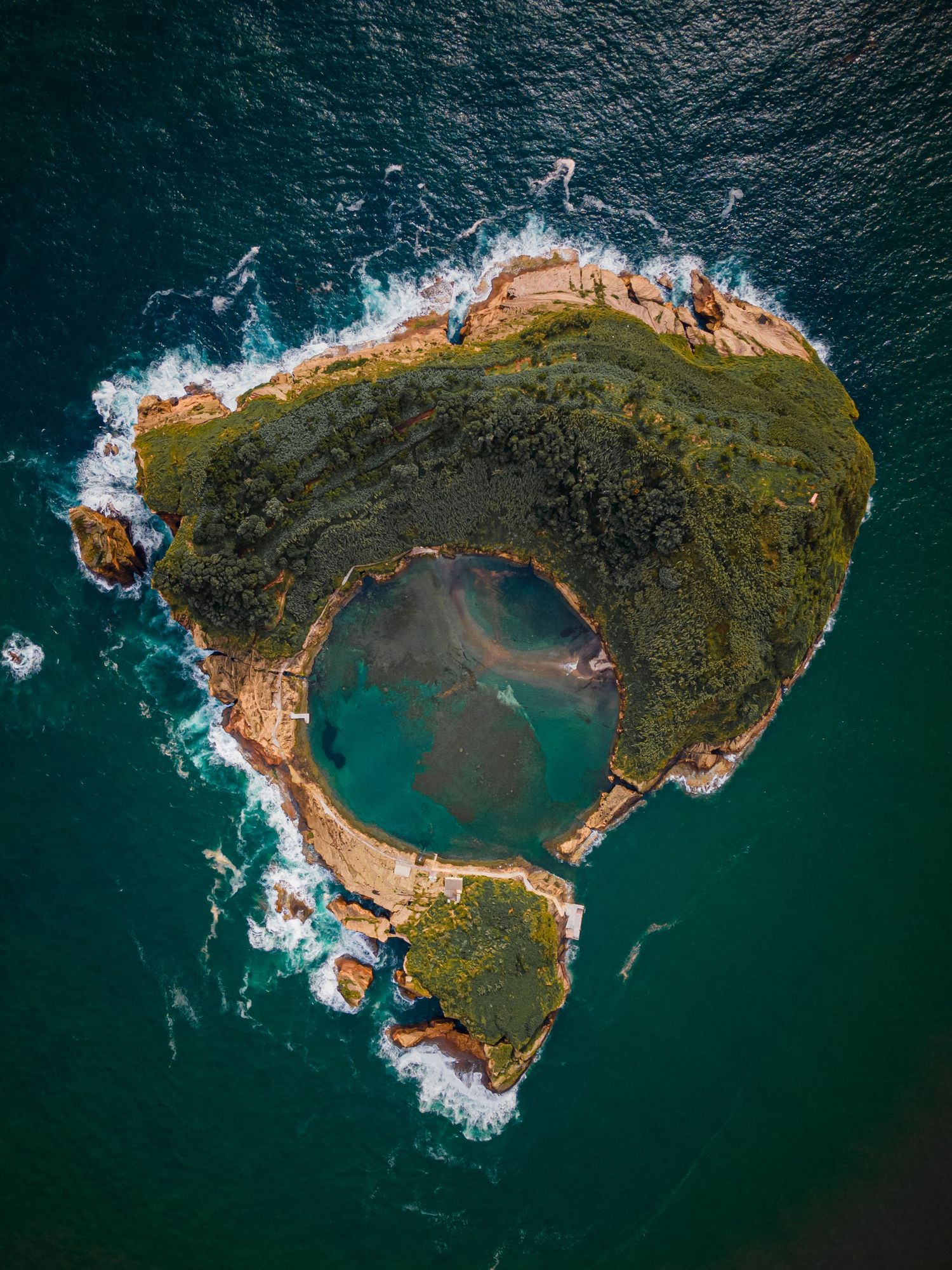 Aerial view of a stunning crescent-shaped volcanic island with turquoise lagoon and rugged coastline surrounded by deep blue sea.