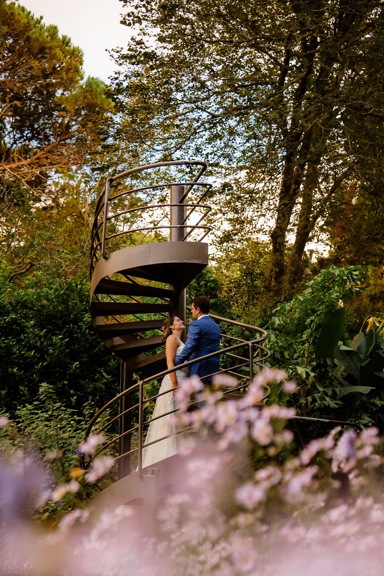 A romantic spiral staircase surrounded by lush greenery and pink flowers in a garden in Terra Nostra Garden on São Miguel, Azores