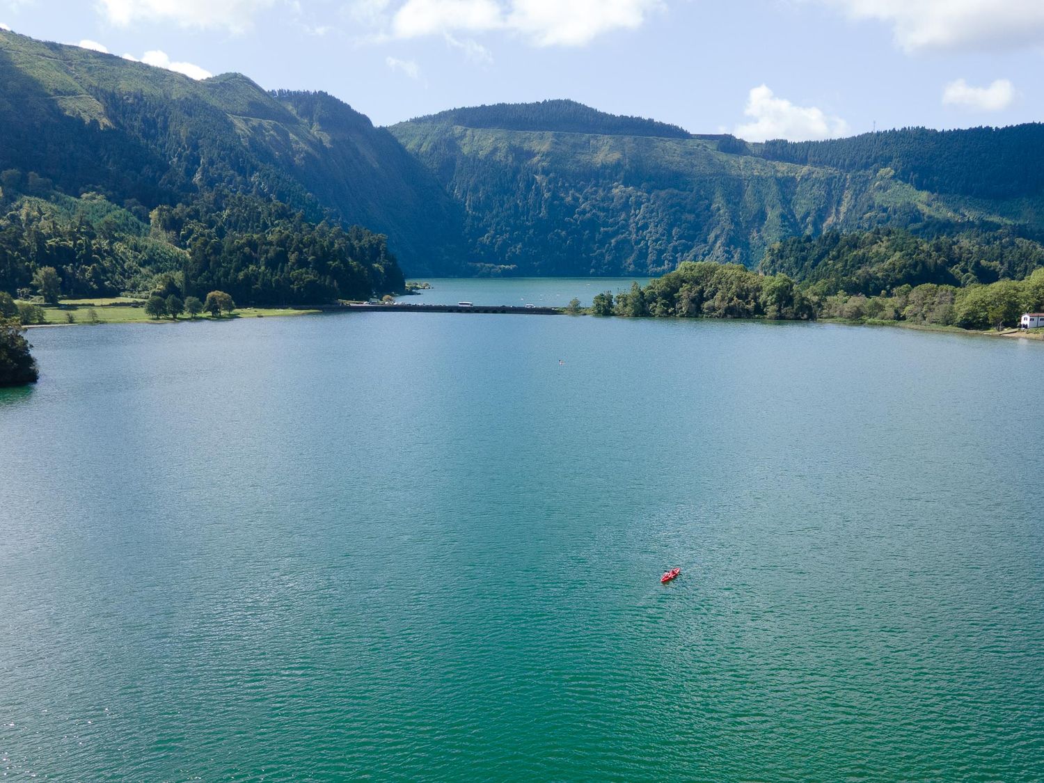 Turquoise lake waters surrounded by green mountain slopes and volcanic cliffs in the Azores islands.