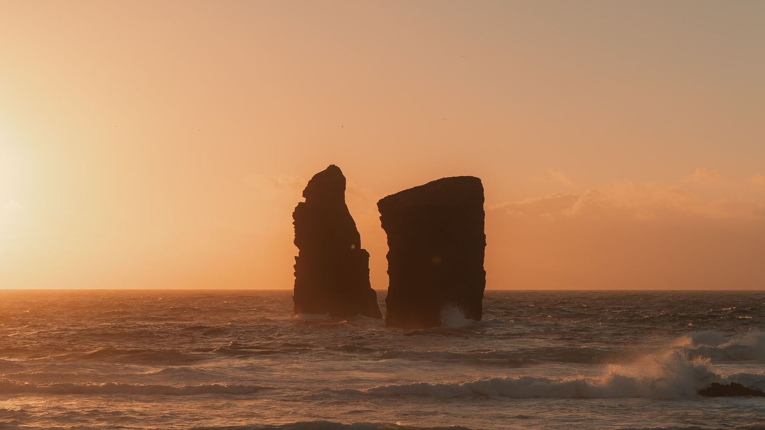 Beautiful orange and purple sunset panorama over rocky ocean cliffs with crashing waves along the Pacific coastline.