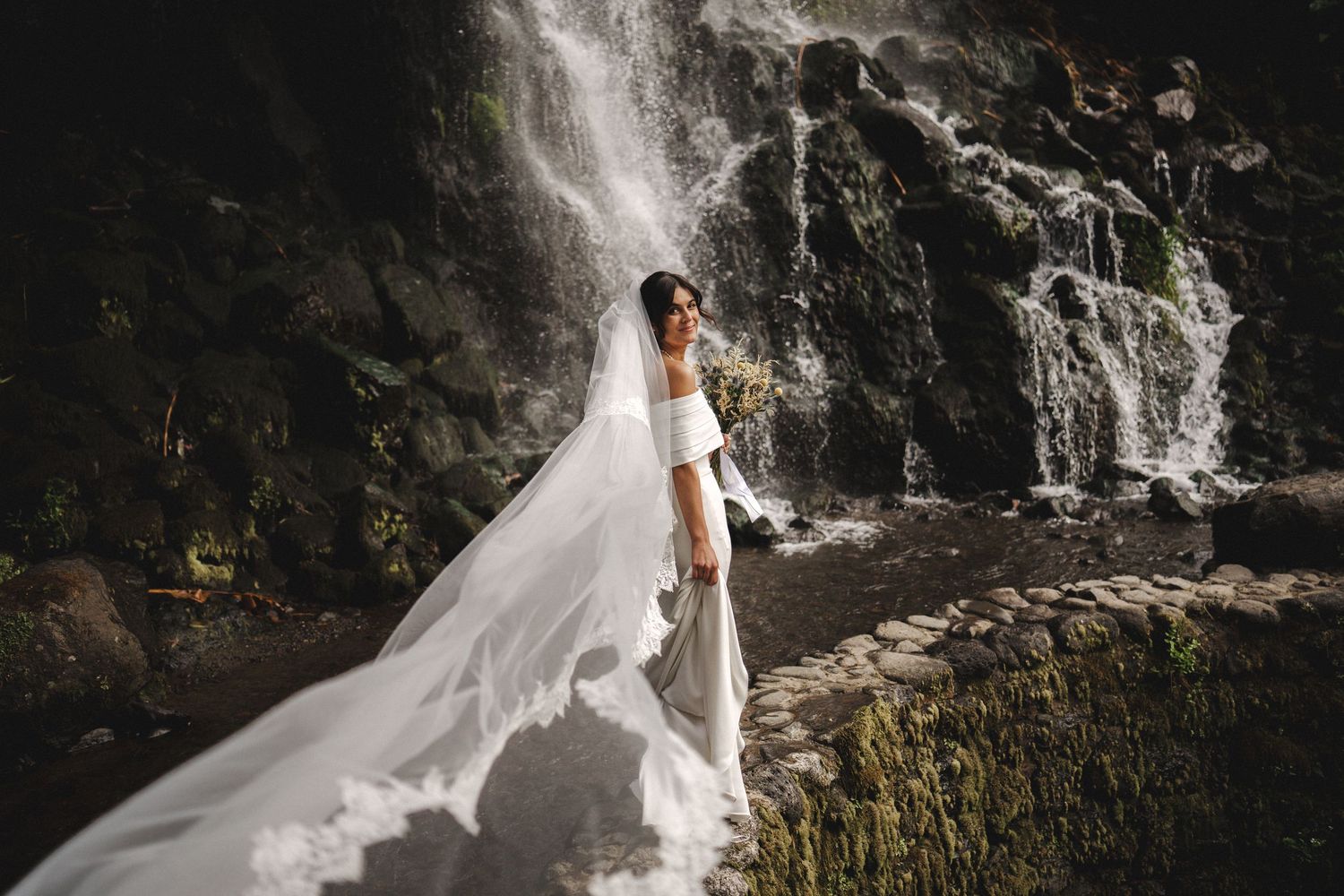 Bride standing by waterfall in São Miguel – wild elopement moment captured by Azores wedding photographer