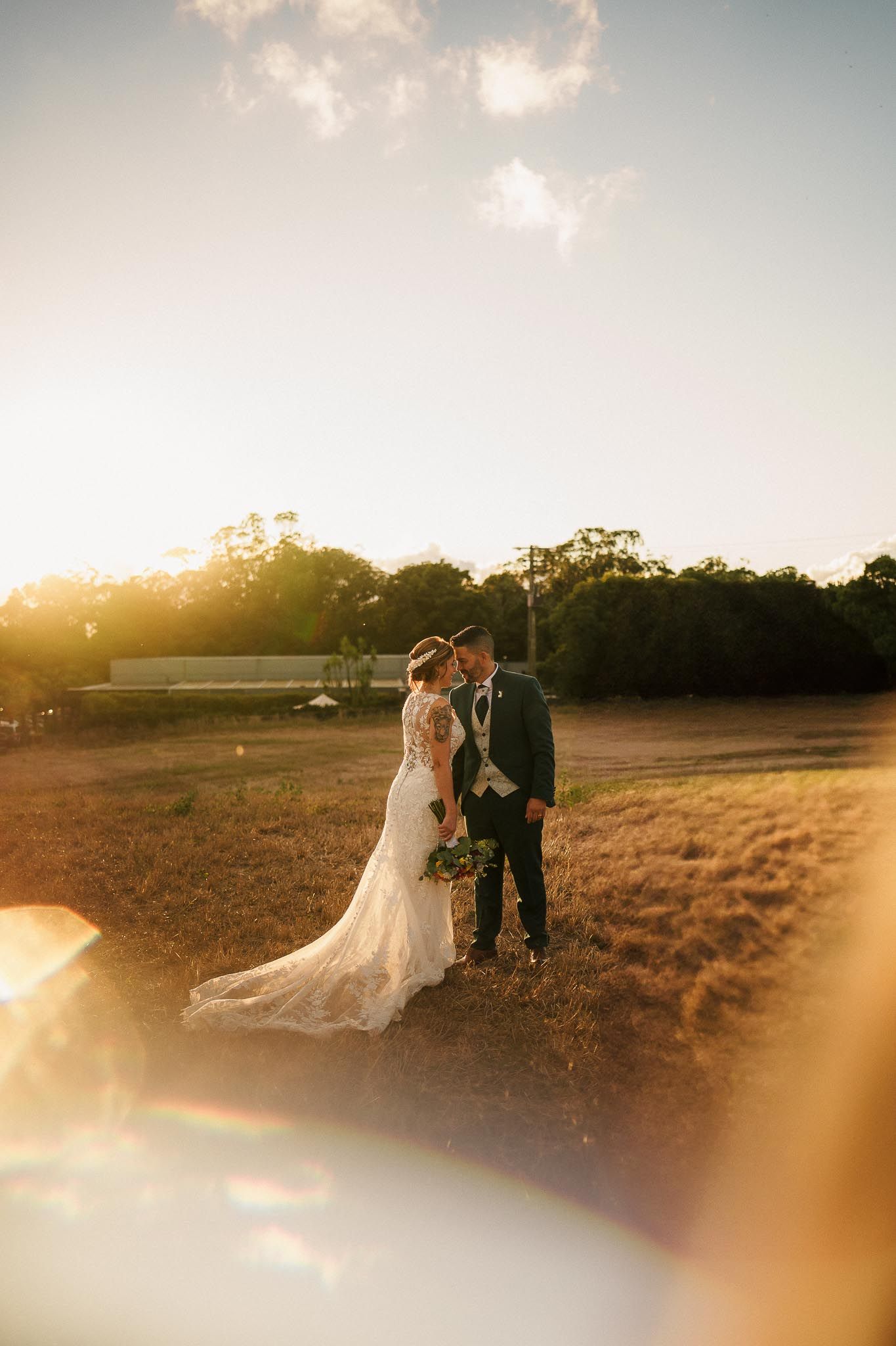 A couple shares an intimate sunset moment in an open field with golden light and long shadows stretching across the grass.
