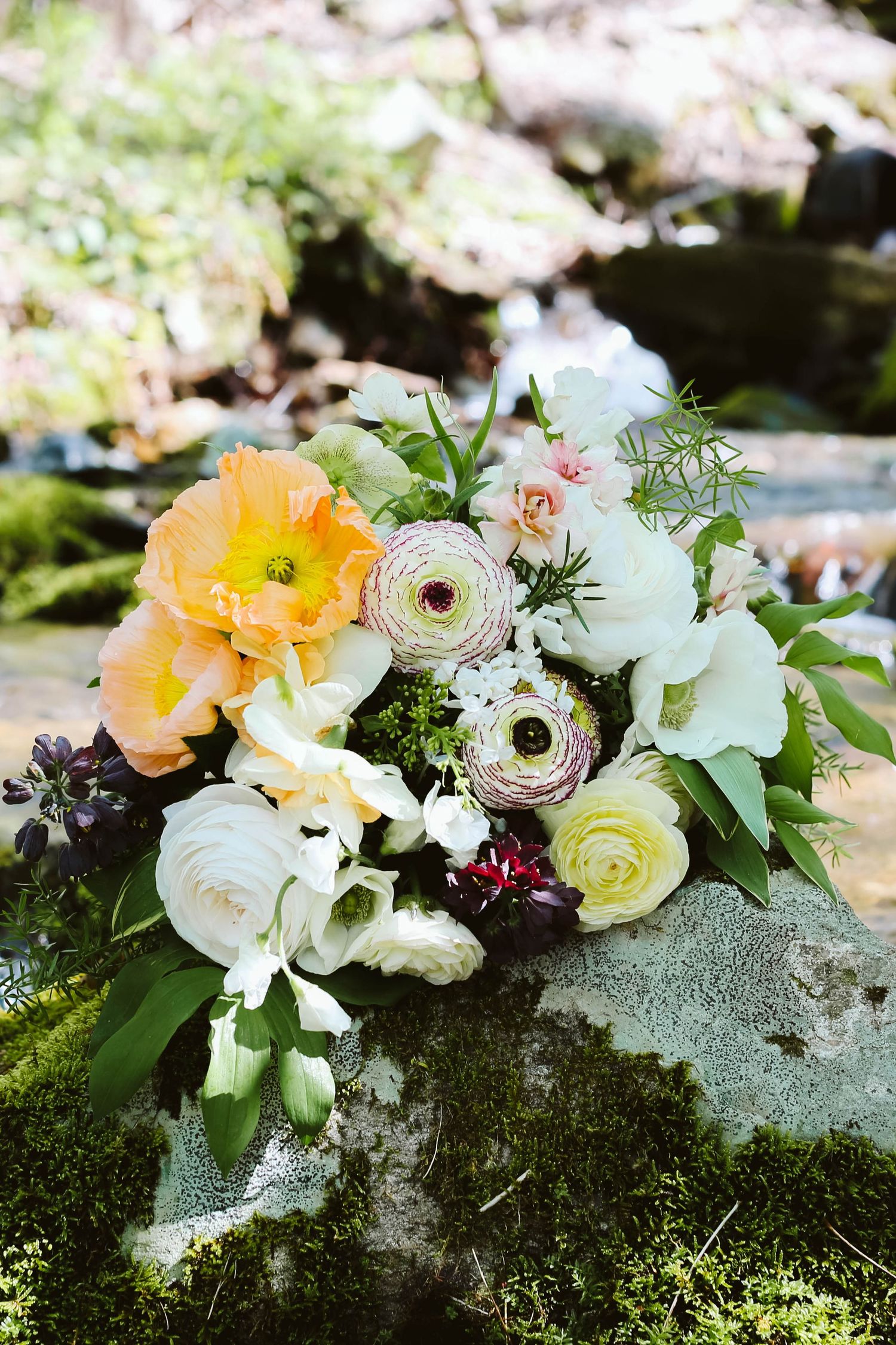 Elegant floral arrangement with white and peach blooms nestled on mossy stone.