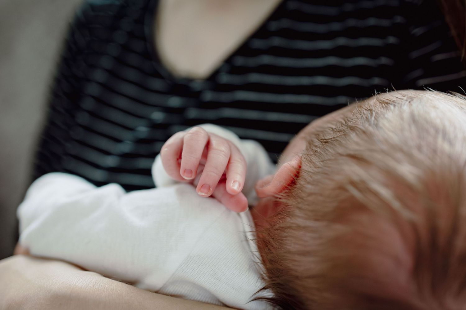 Close-up of a newborn baby breastfeeding, grasping mother's shirt with tiny fingers.