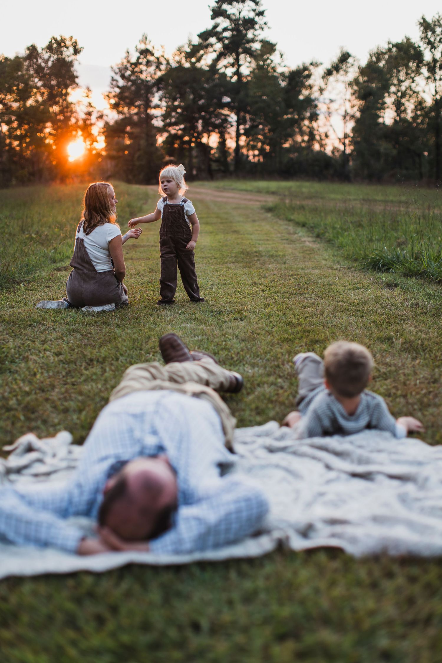 Family enjoying a peaceful sunset picnic on a blanket in a grassy field during golden hour.