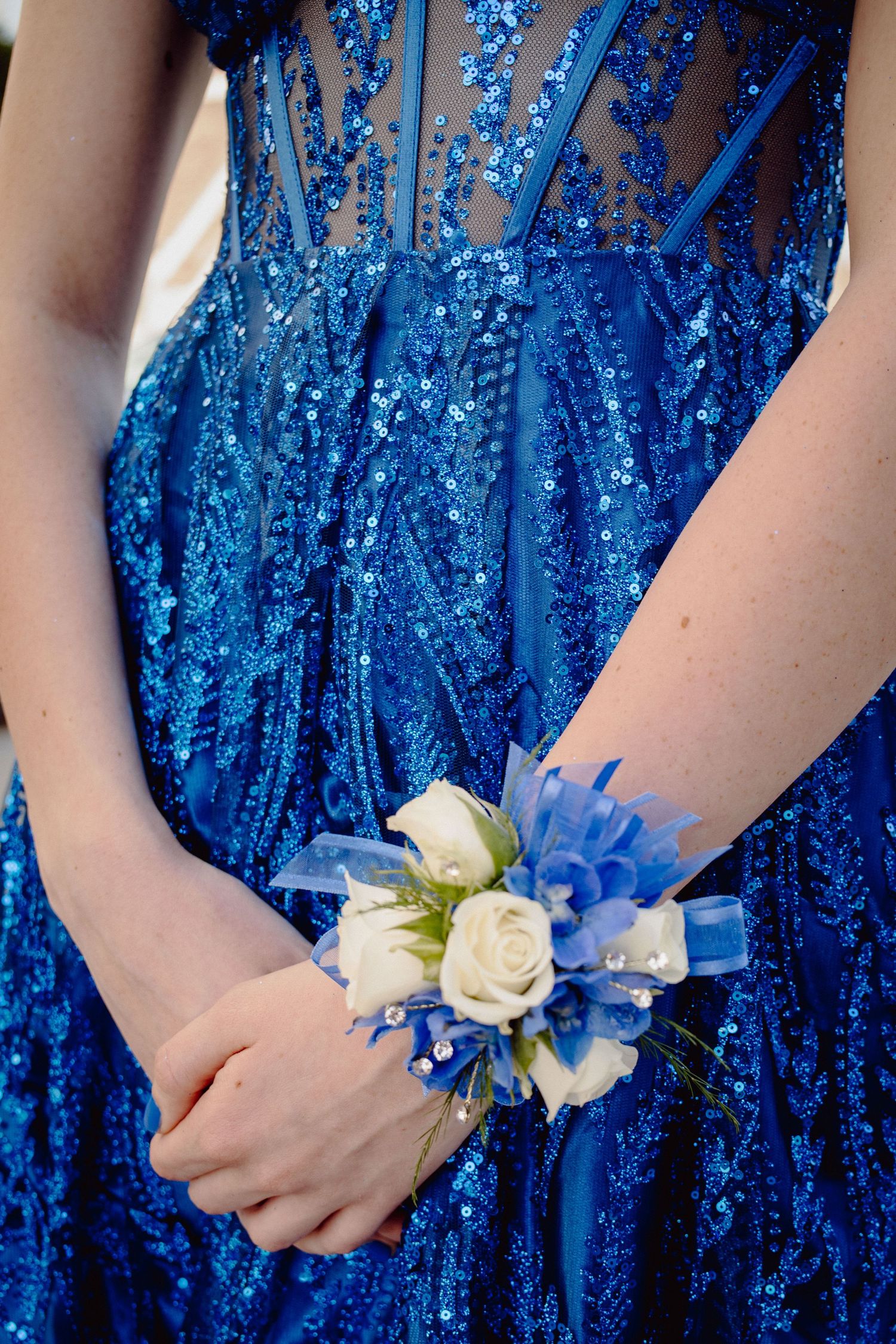 Woman in blue sequin prom dress with white rose and blue ribbon wrist corsage.