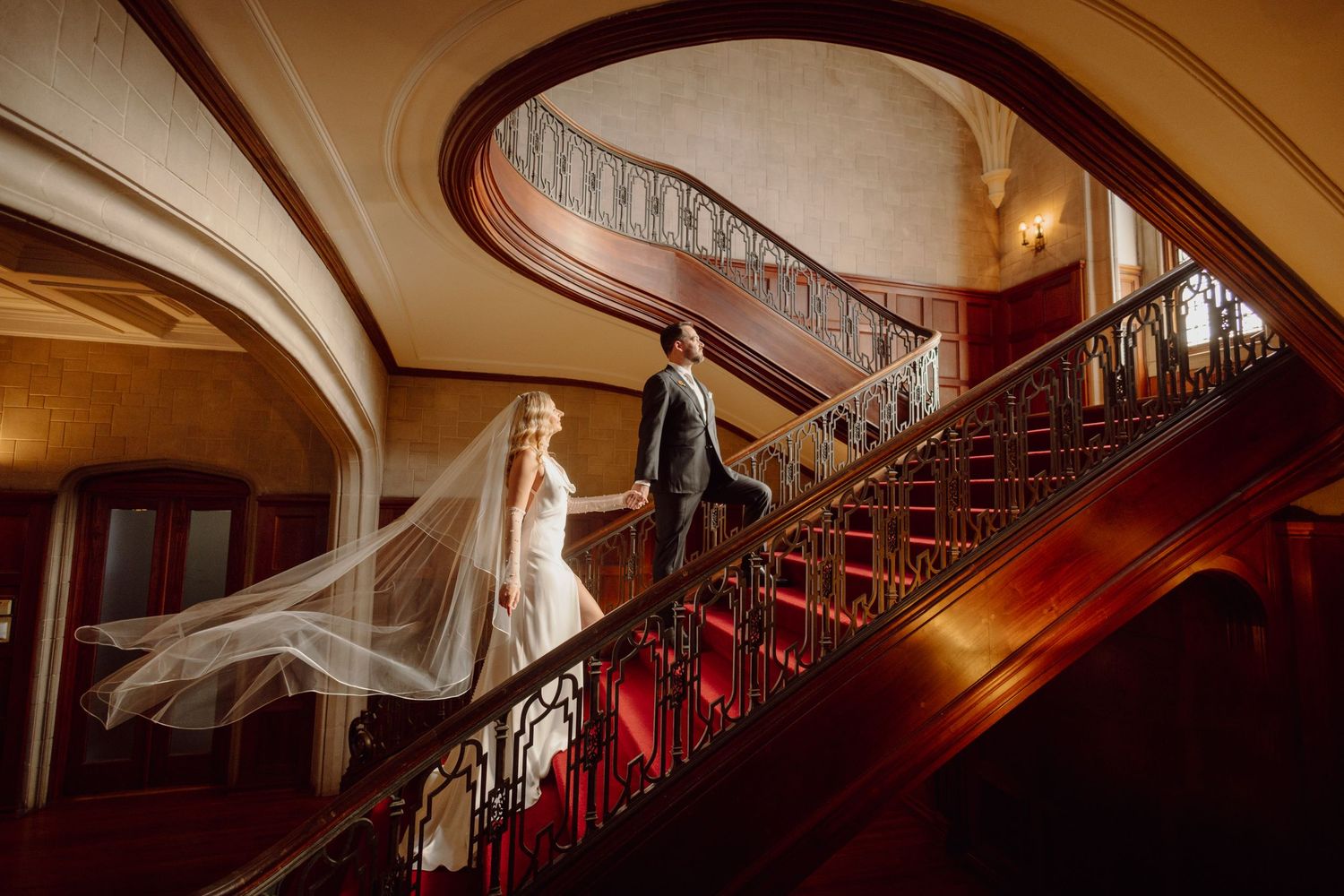 Grand wooden staircase with ornate red carpet and curved banister in historic building interior.