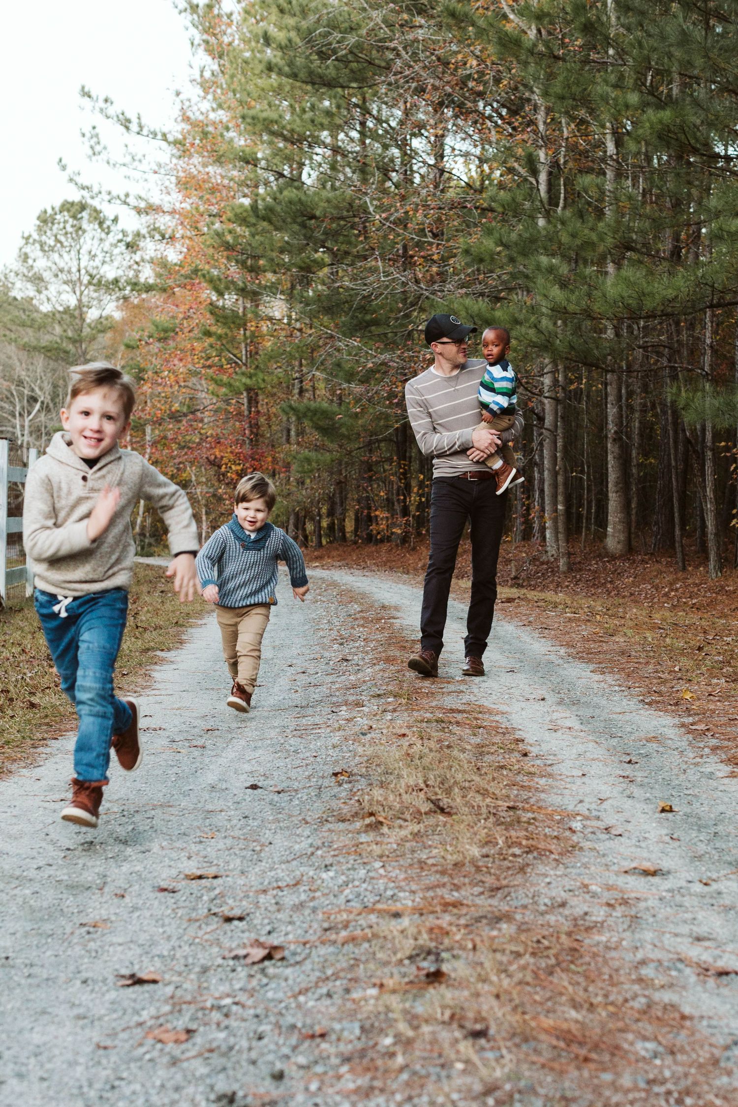 A family enjoys an autumn walk on a gravel path through a pine forest with fall foliage.