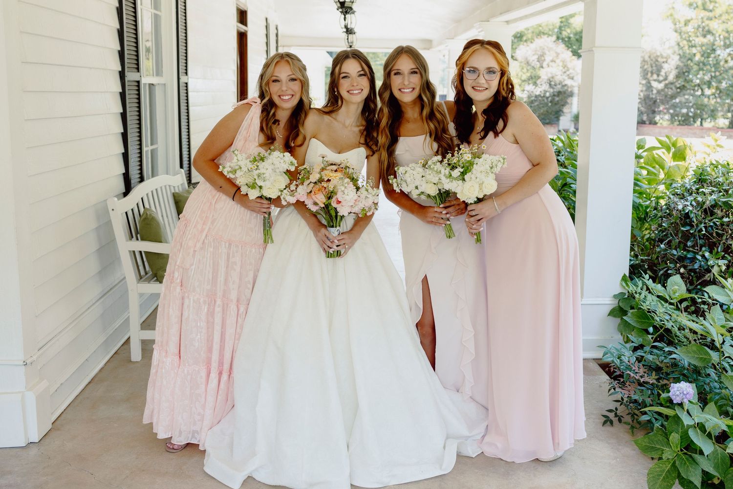 Wedding party in pink bridesmaid dresses and white gowns posing on a white columned porch.