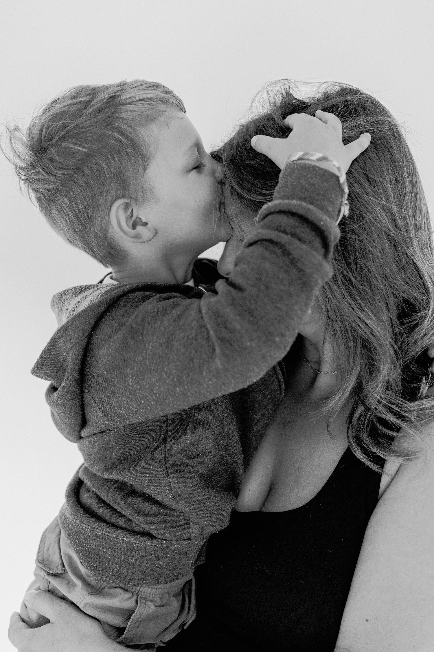 A series of black and white photos showing a toddler in a gray sweater giving kisses to someone in a tender moment.