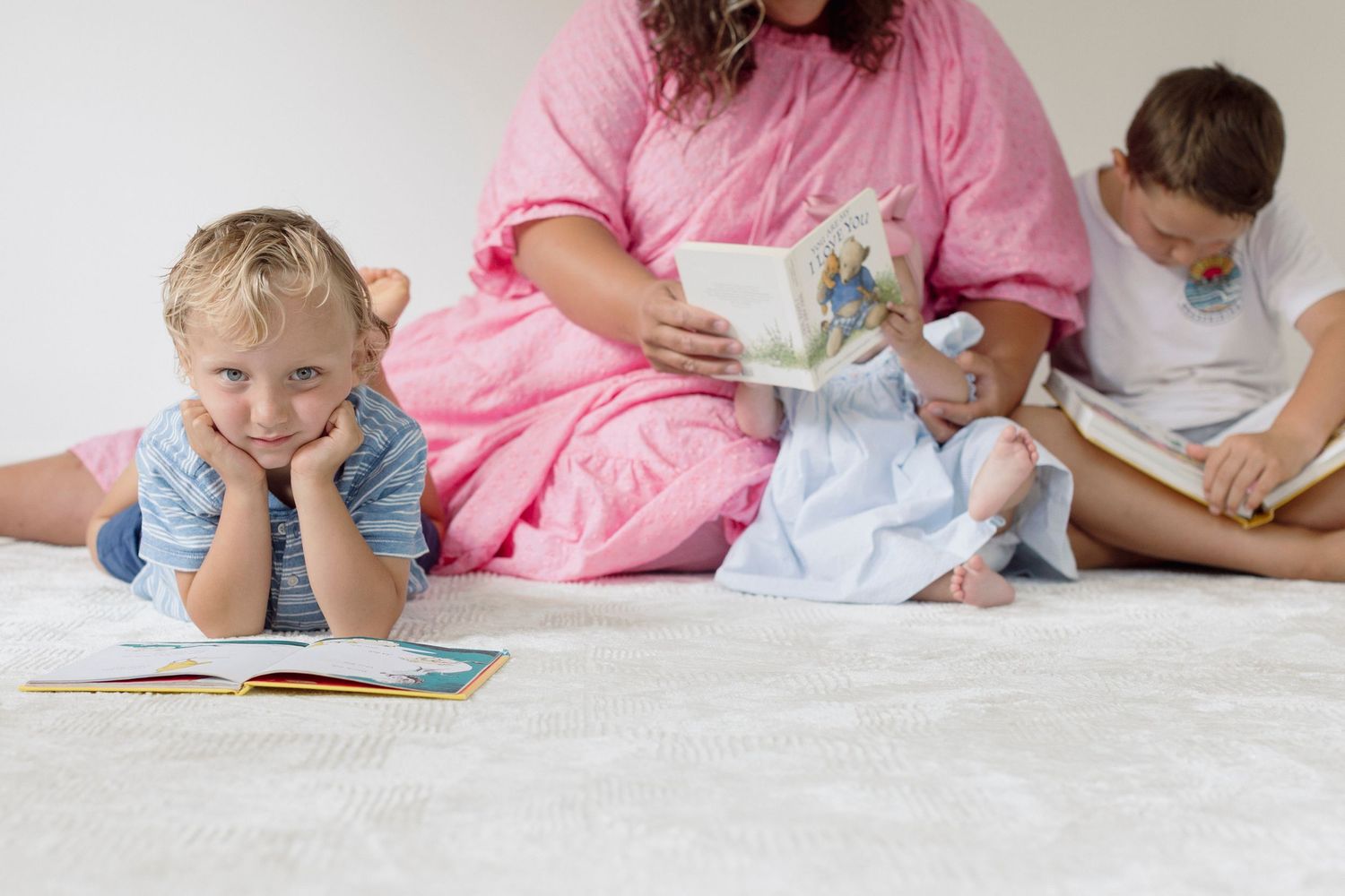 Family reading books together while relaxing on white carpet at home.