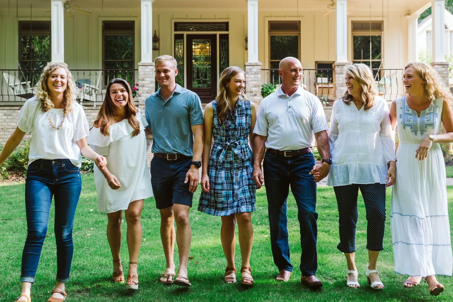 Large group of people standing in line on green grass wearing coordinated white and blue summer outfits.