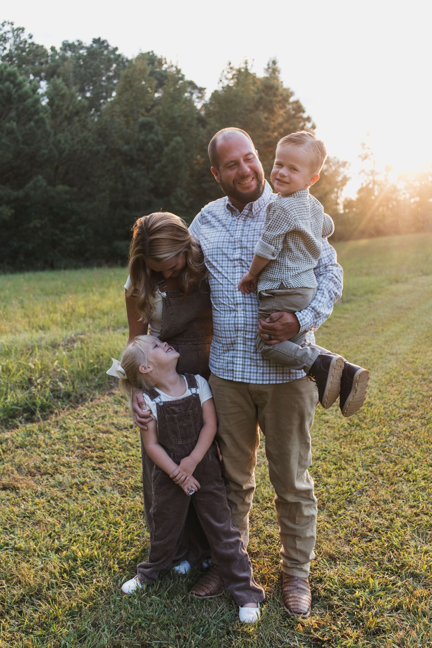 A family shares tender moments together in a sunlit grassy field during golden hour.