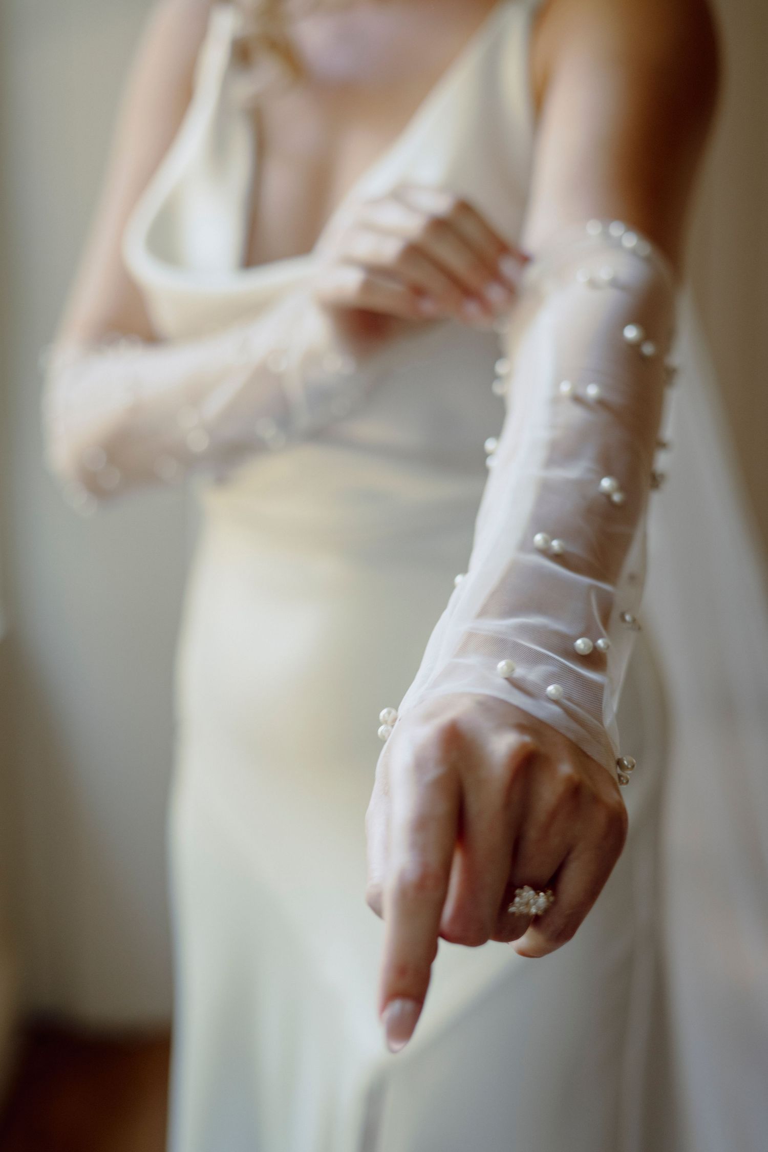 Close-up details of pearl buttons on sheer white wedding dress sleeve.