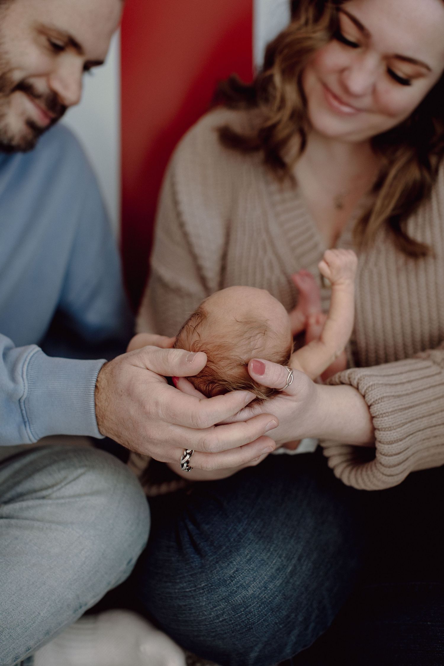 Parents tenderly holding their newborn baby's tiny hand in an intimate indoor portrait with warm lighting.