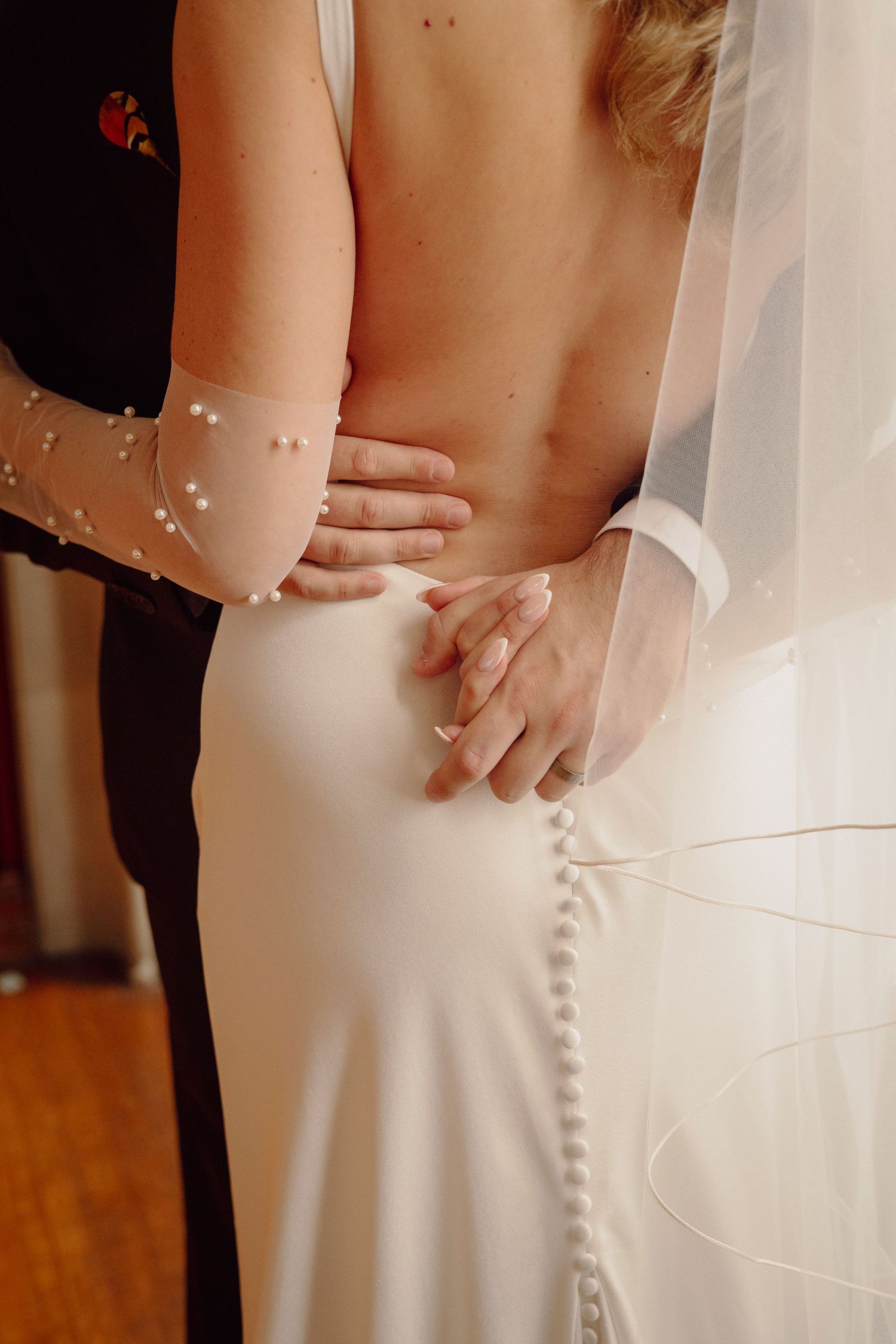 Detail shot of buttons down the back of a sleek white wedding dress with veil.