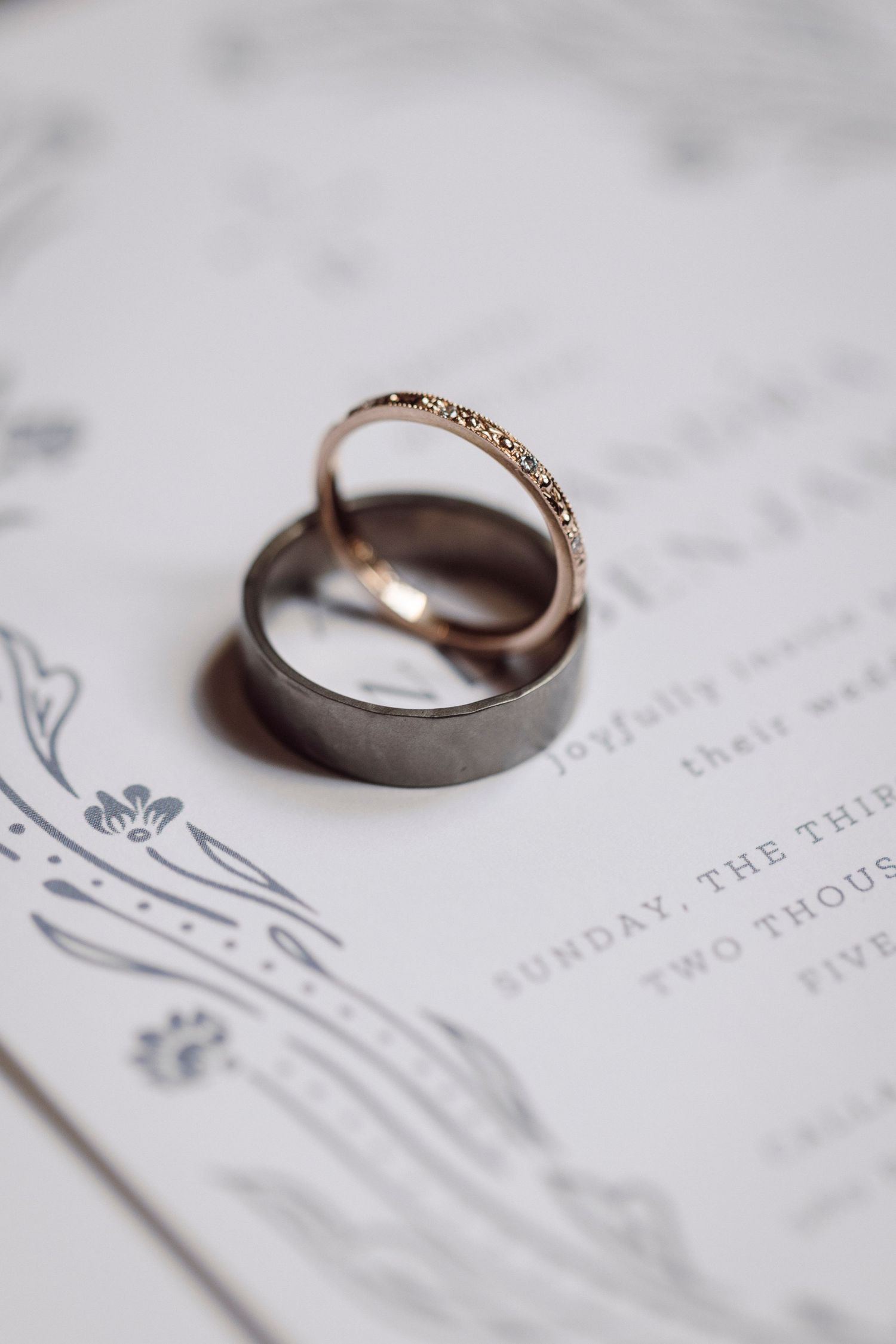Wedding rings photographed on elegant wedding invitation with floral design details.