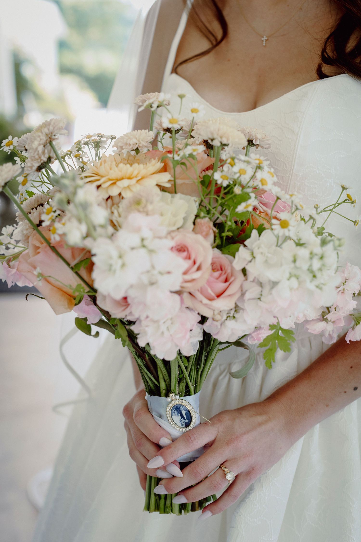 Delicate pink and white floral wedding bouquet wrapped in white fabric with a vintage brooch accent.