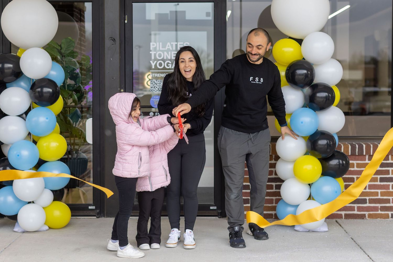 A festive balloon garland installation in blue, white, and yellow colors decorates the entrance of a brick building.
