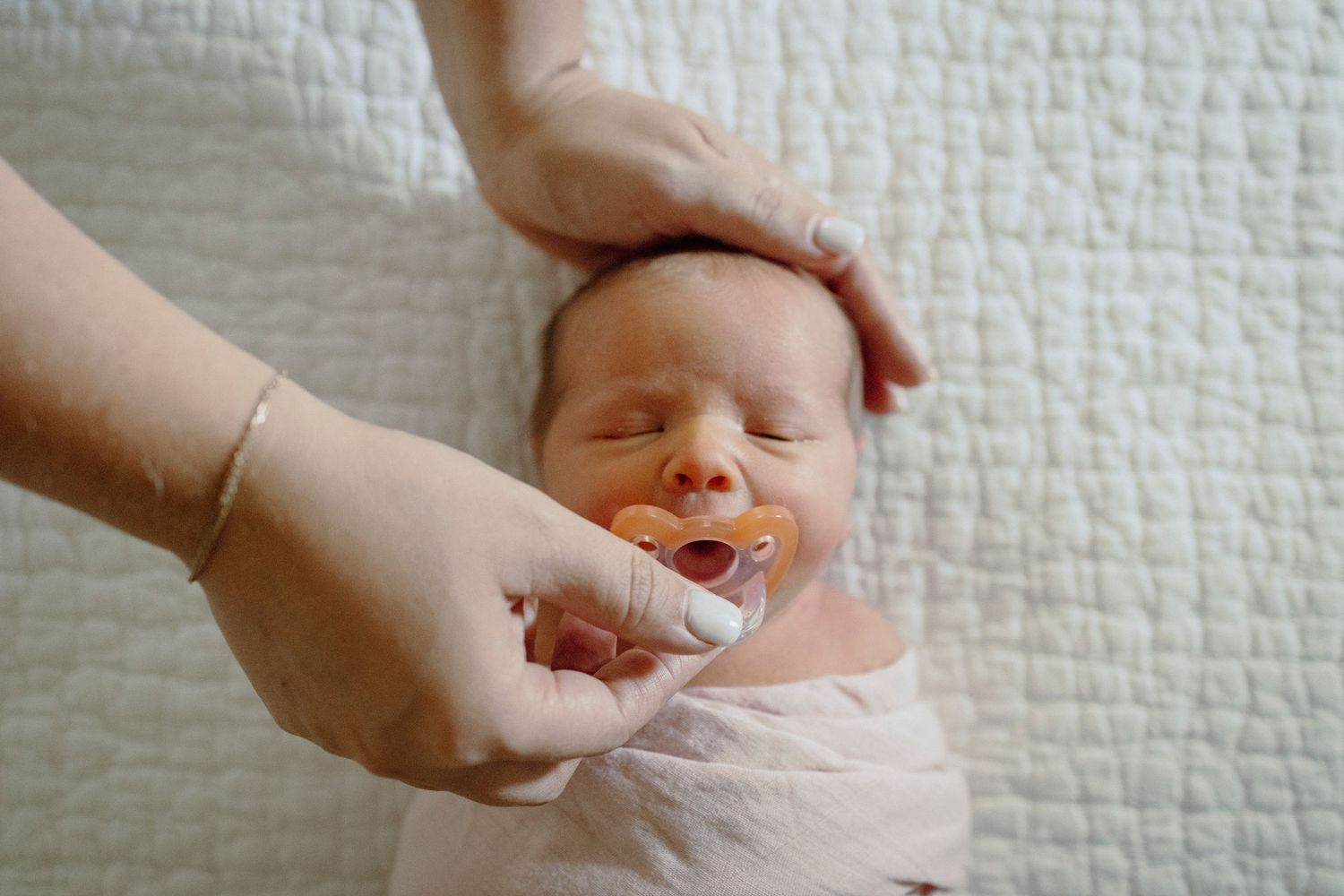 A series of photos showing hands swaddling a sleeping baby in a soft white blanket.