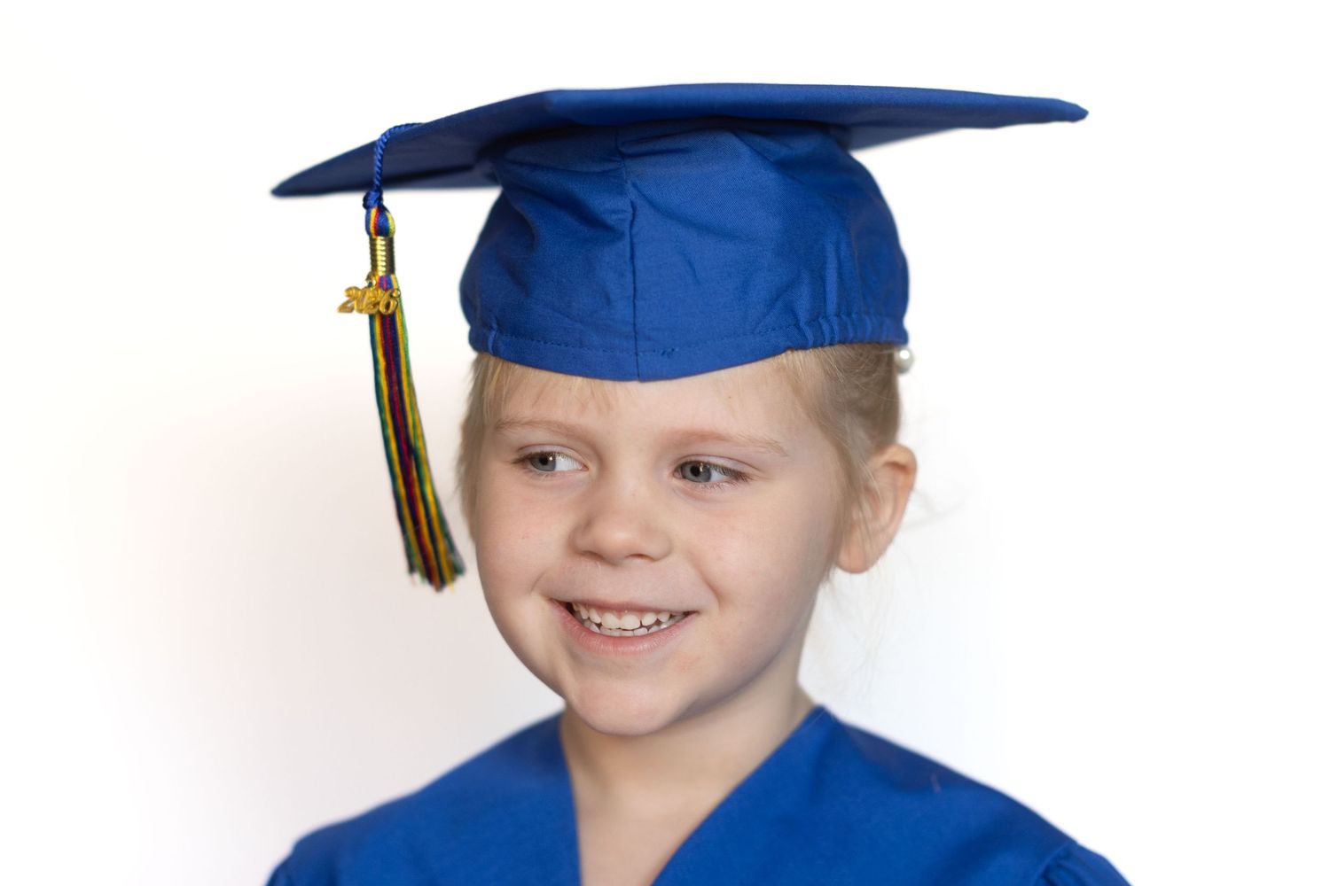 Young girl smiling in blue graduation cap and gown, celebrating kindergarten or preschool graduation.