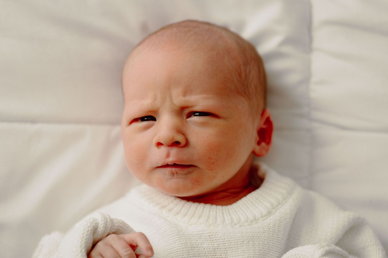 A newborn baby lies on white bedding in a series of close-up photos showing different expressions.