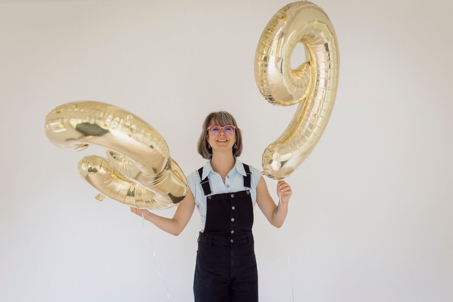 Person posing with large gold metallic number balloons in studio setting.